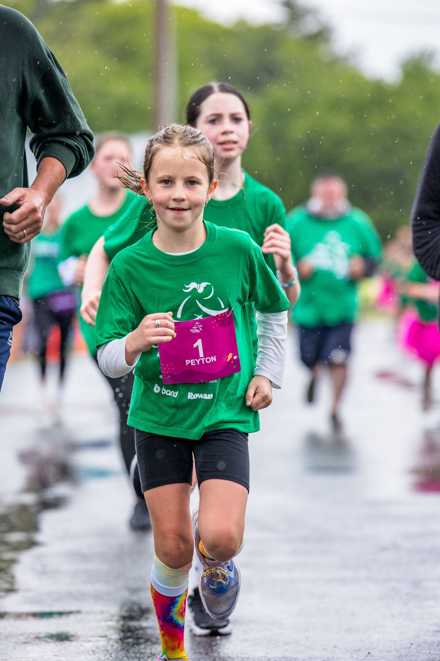 Young girl named Peyton wearing green shirt and pink bib running in a charity race on a rainy day.