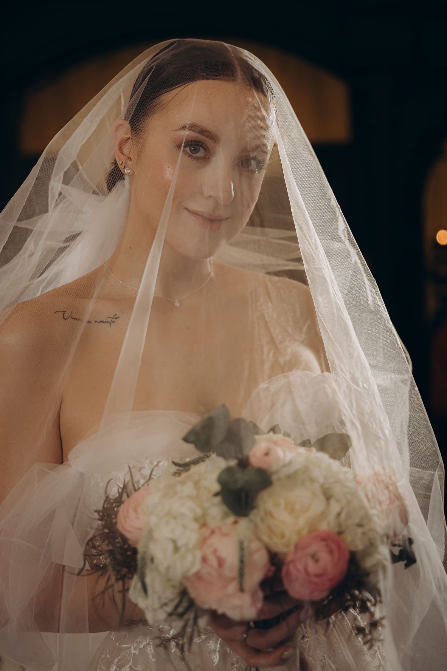 Soft portrait of a bride under a translucent veil holding a bouquet. By Julia Tris.