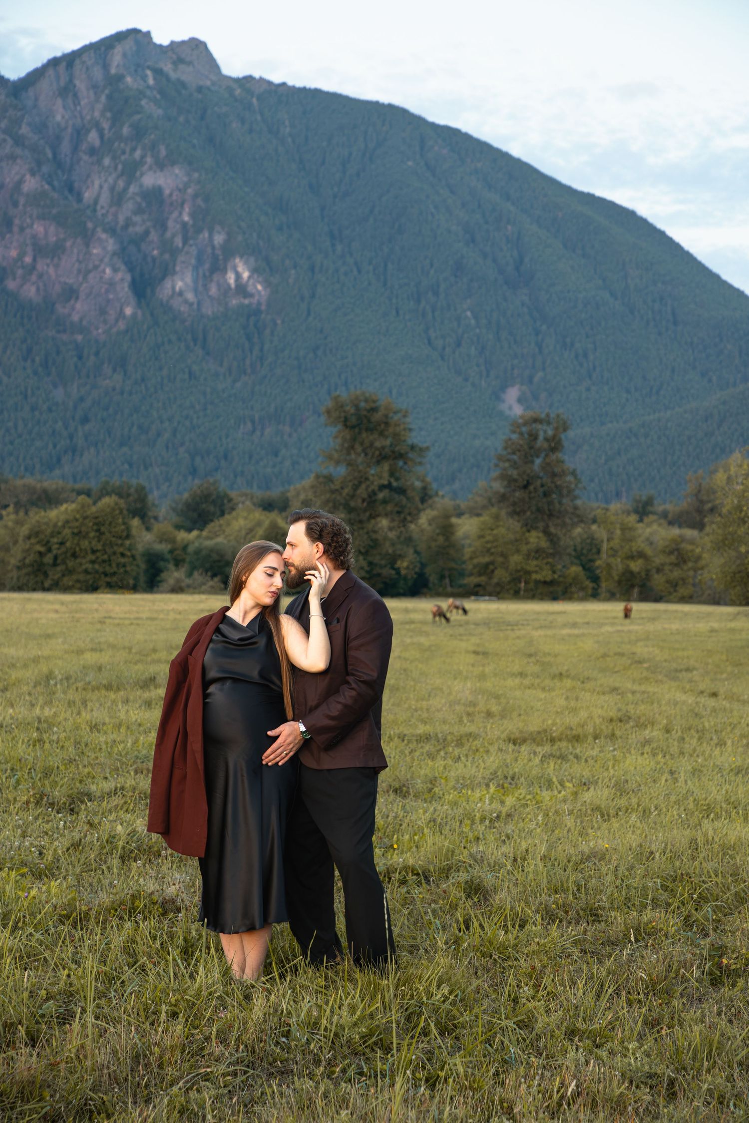 Expectant couple embracing in an open field with Mount Si rising behind them in North Bend