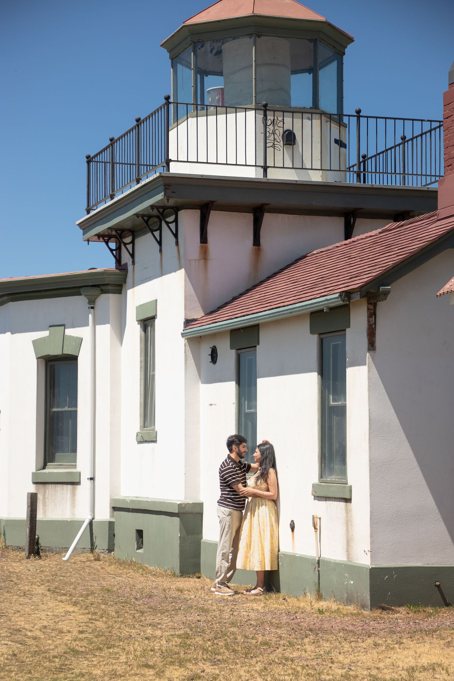 Newly engaged couple embracing beside West Point Lighthouse at Discovery Park in Seattle