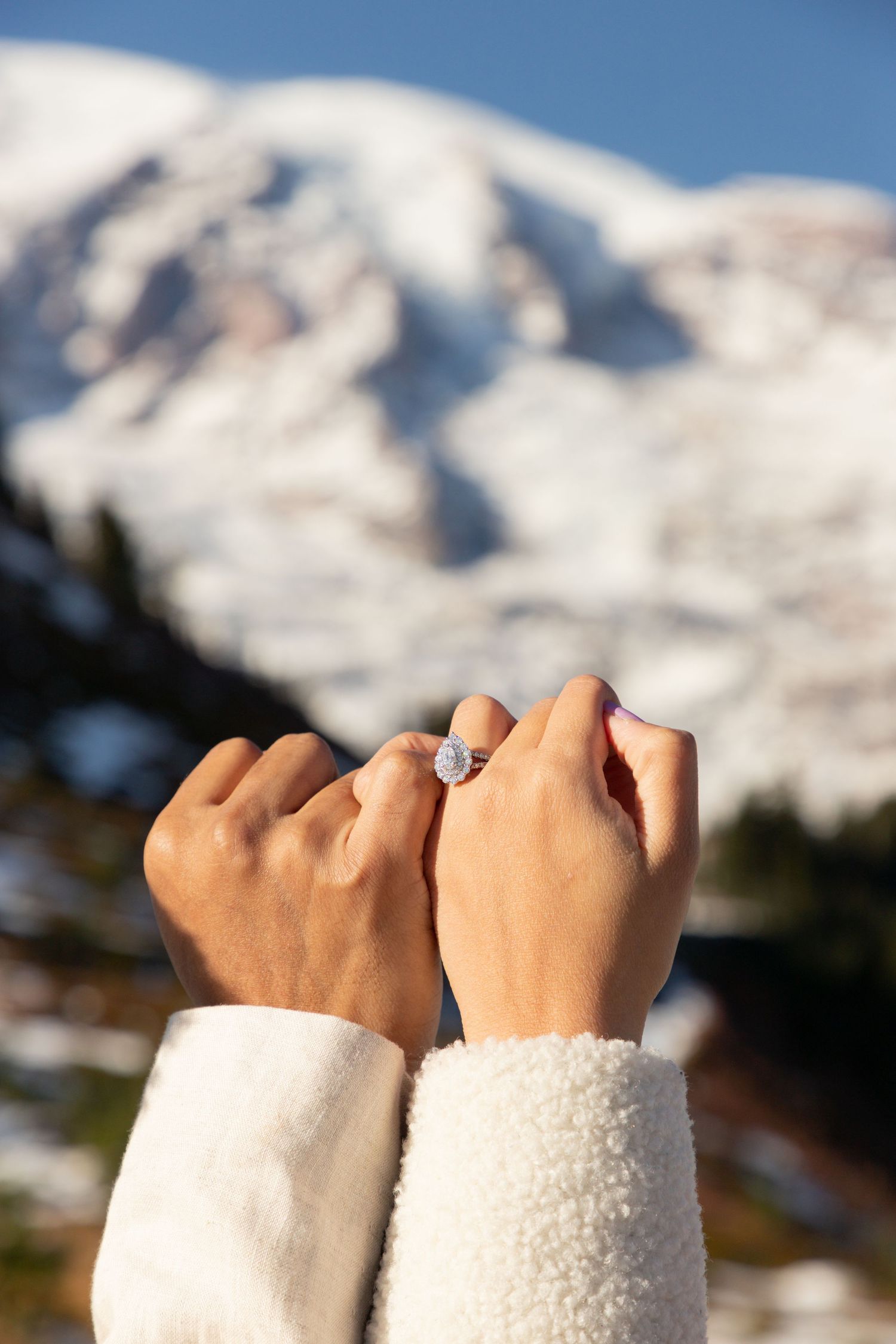 Close‑up of an engagement ring on a couple’s hands with Mount Rainier in the background during an engagement photoshoot