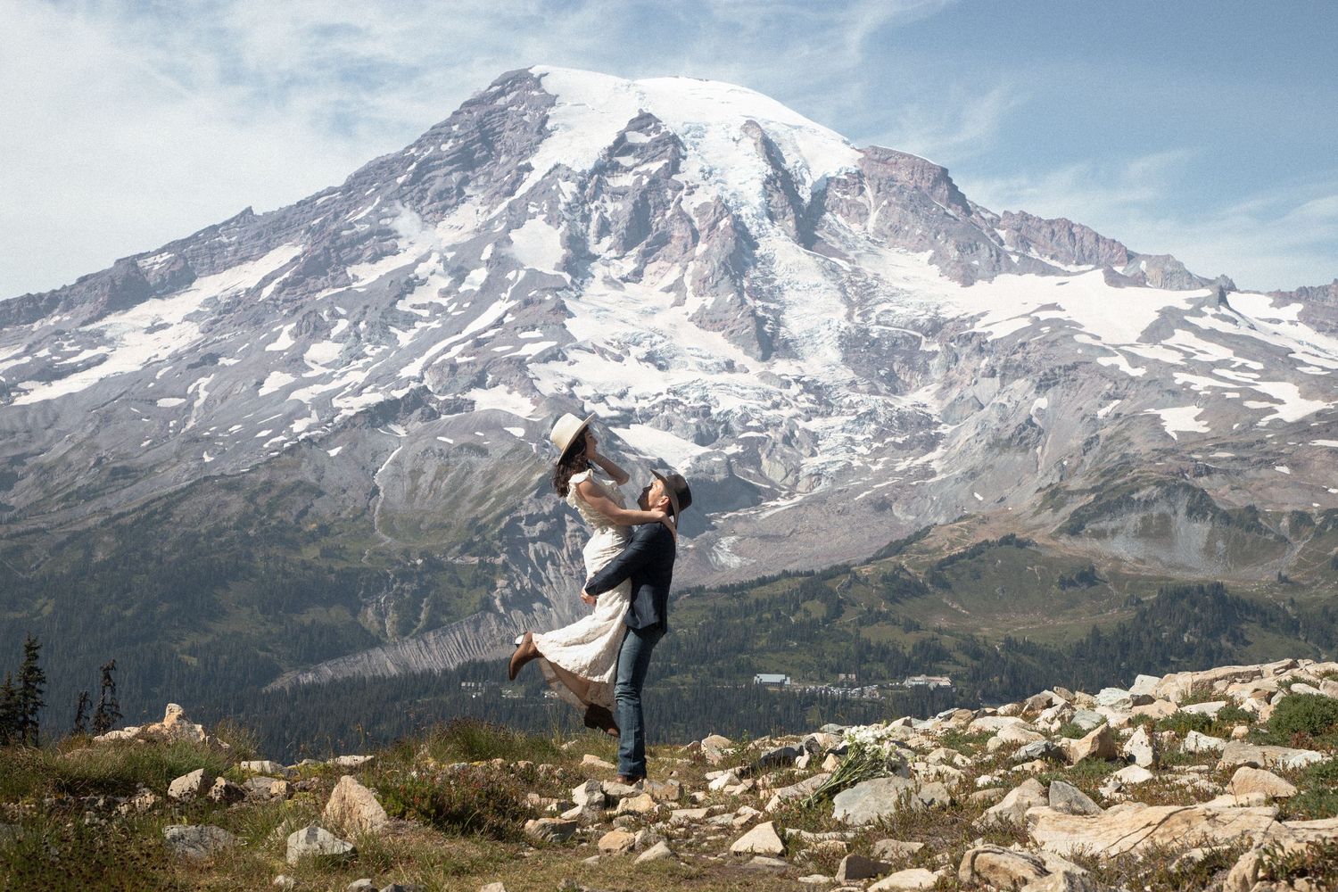 Groom lifting the bride on a rocky overlook with Mount Rainier filling the background