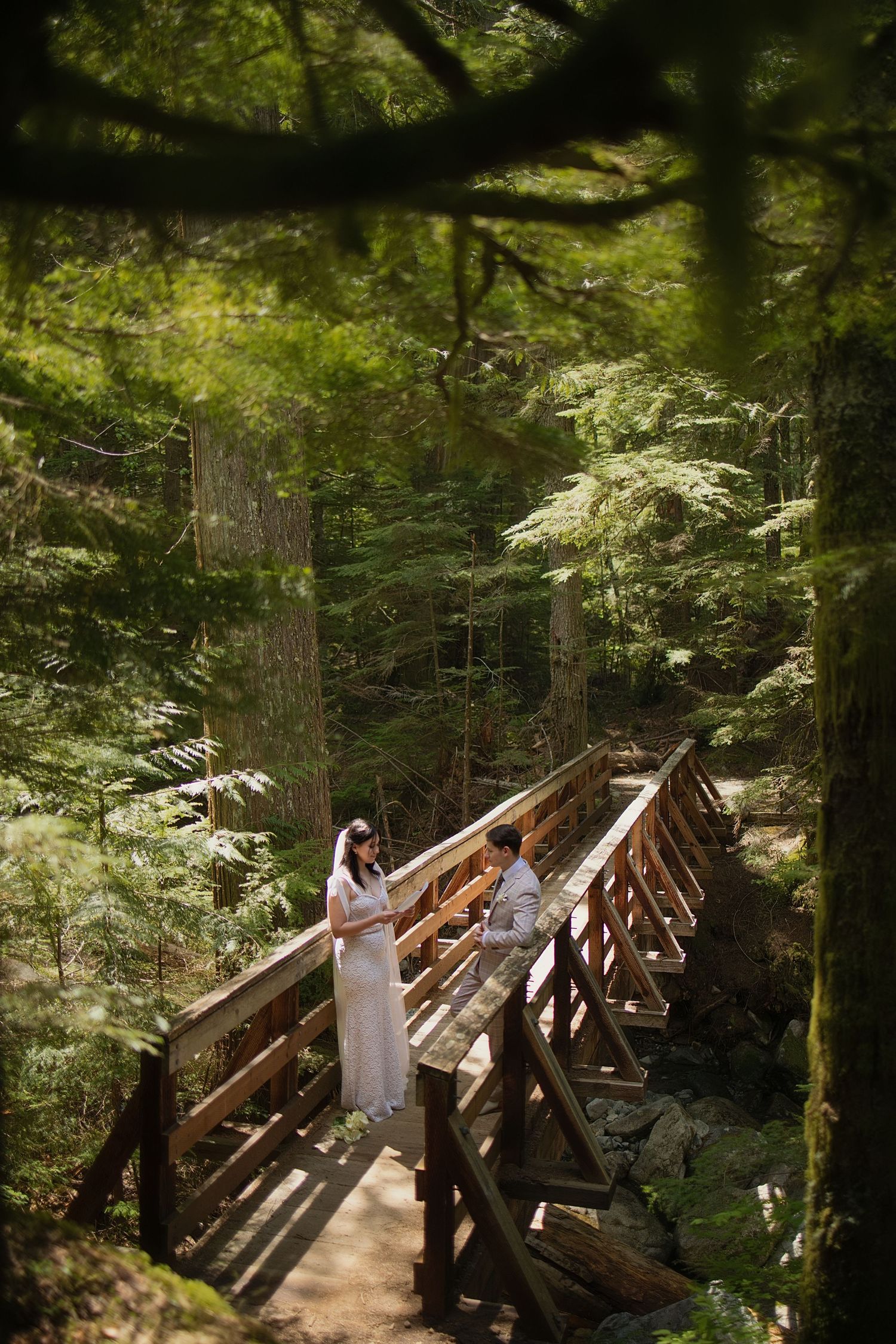 Bride and groom reading their vows on a wooden bridge surrounded by Pacific Northwest forest