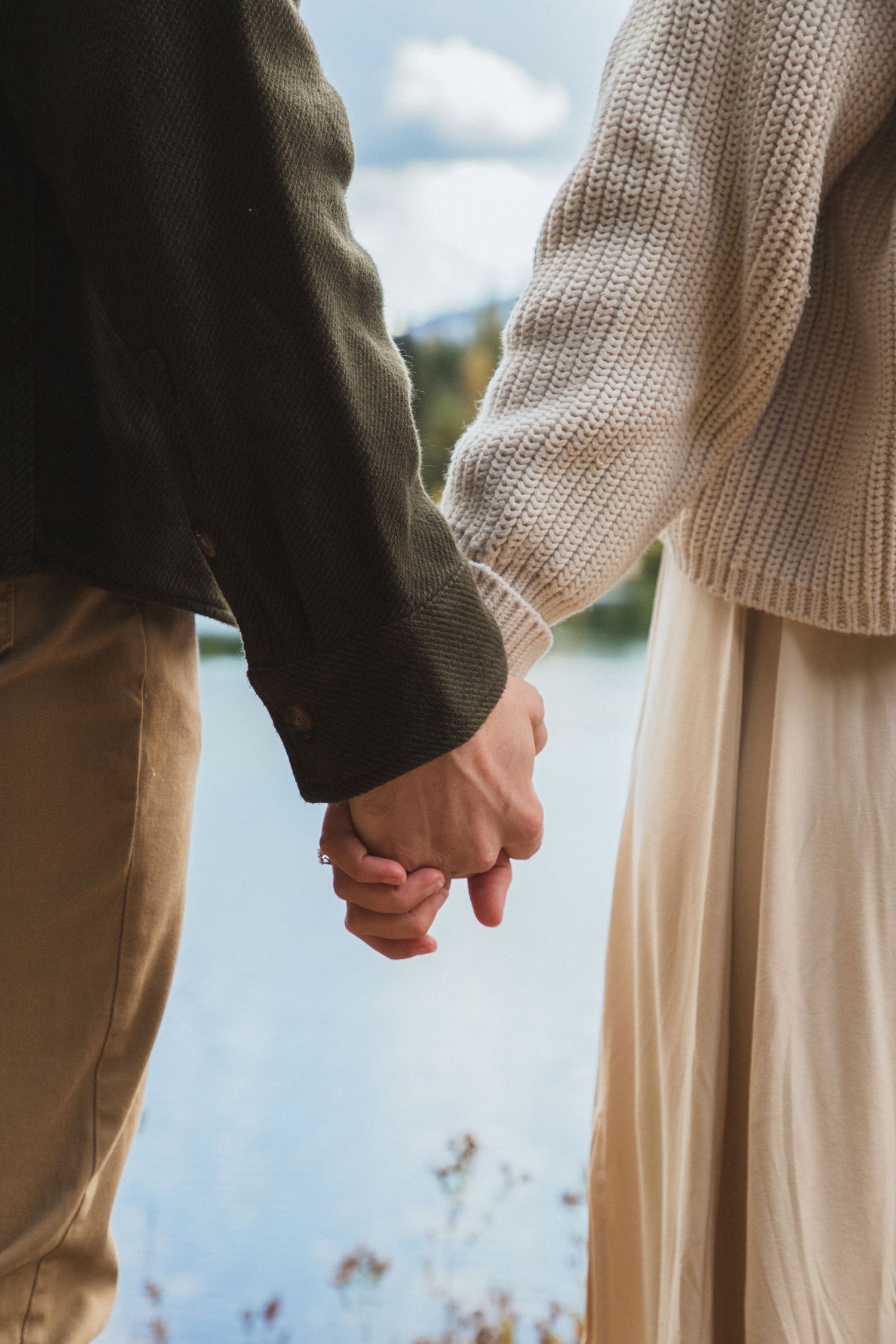 Close‑up of a couple holding hands with Gold Creek Pond in the background during a photoshoot