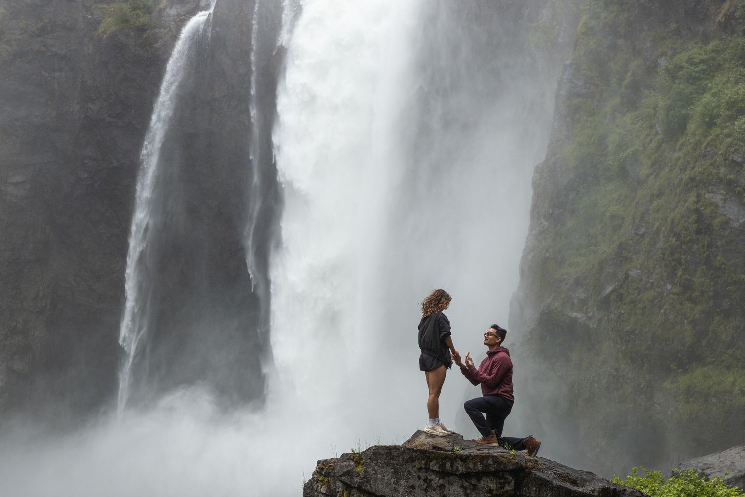 Man proposing on one knee in front of Snoqualmie Falls during a surprise proposal photoshoot