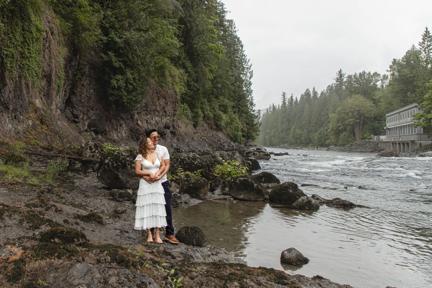 Newly engaged couple posing together on the rocky riverbank near Snoqualmie Falls