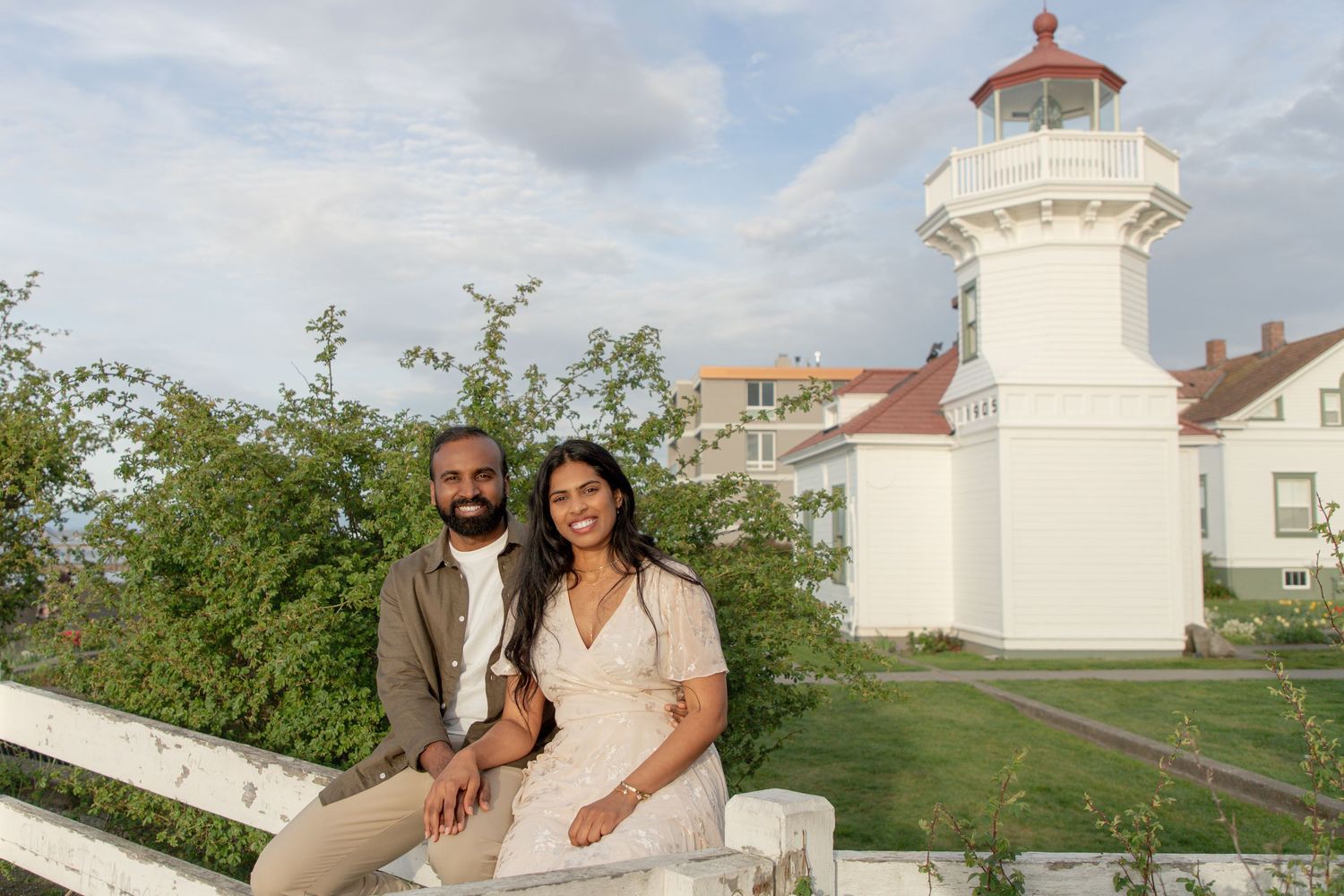Newly engaged couple sitting together with Mukilteo Lighthouse in the background