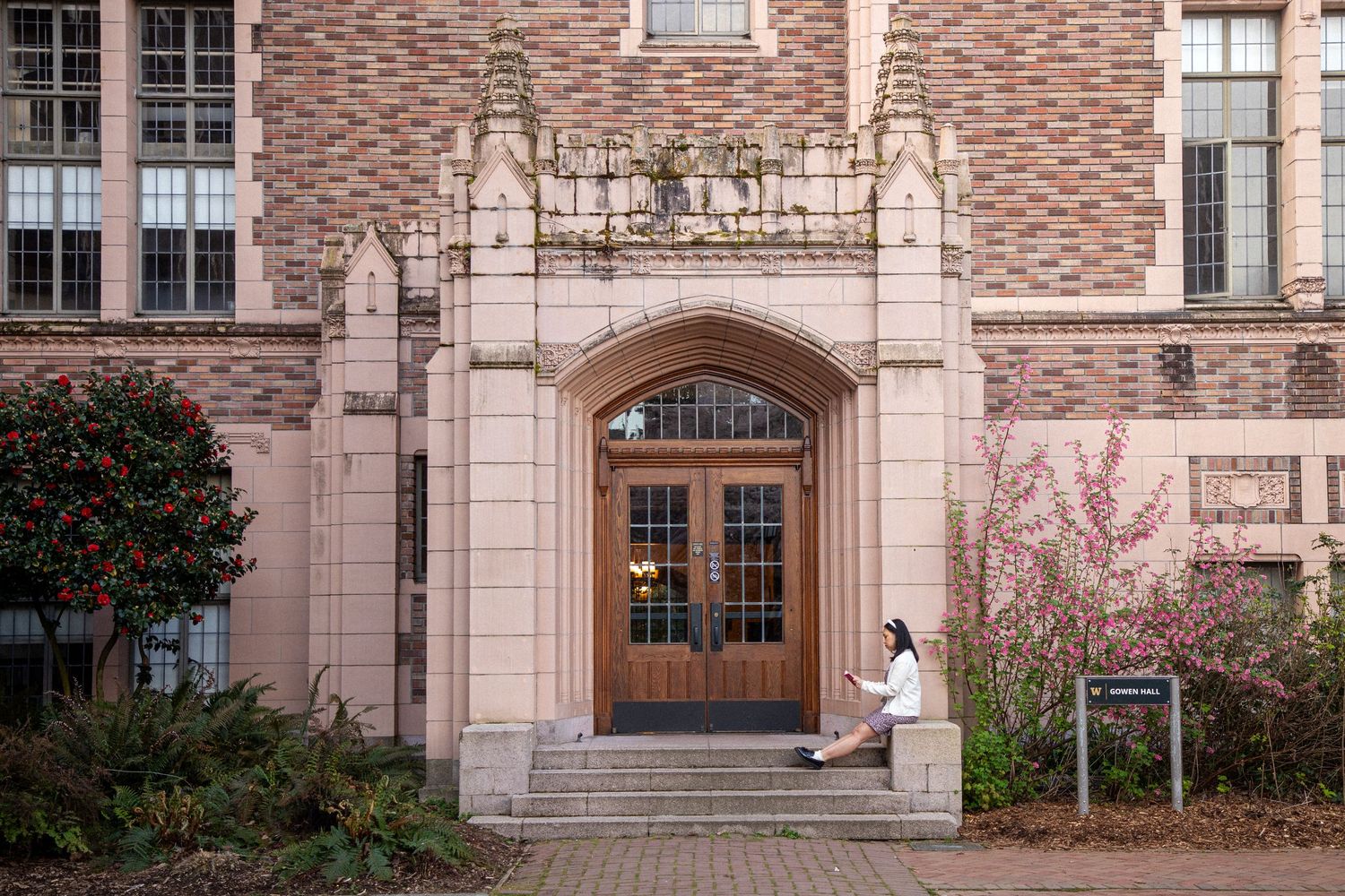 Woman sitting outside a historic building during a cherry blossom portrait session at the University of Washington in Seattle