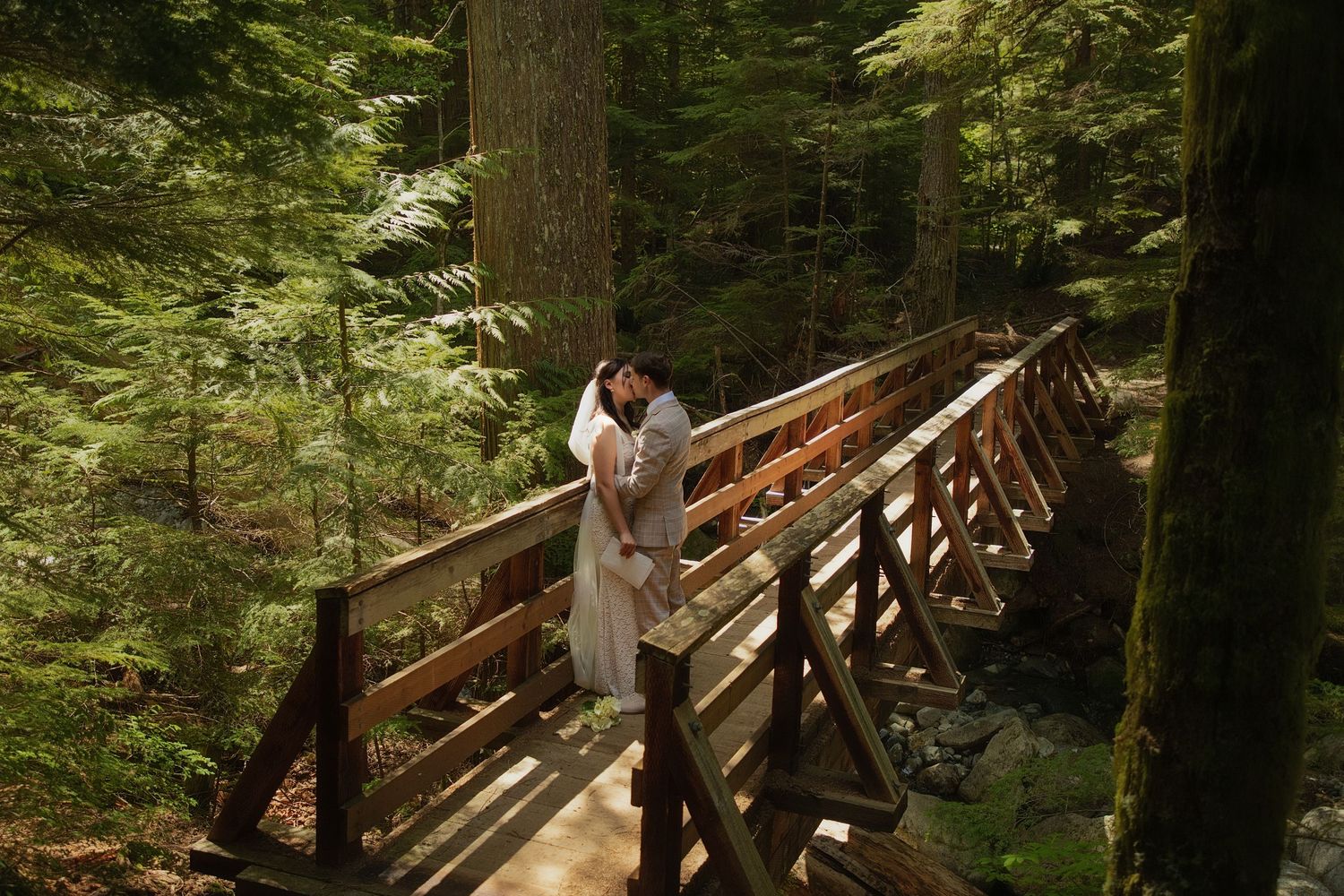 Bride and groom kissing on a wooden bridge during an intimate forest elopement in Washington State