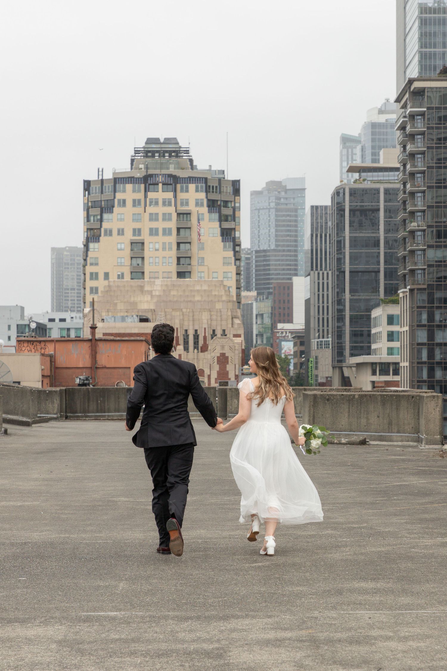 Newlywed couple running across a downtown Seattle rooftop after their intimate courthouse wedding ceremony
