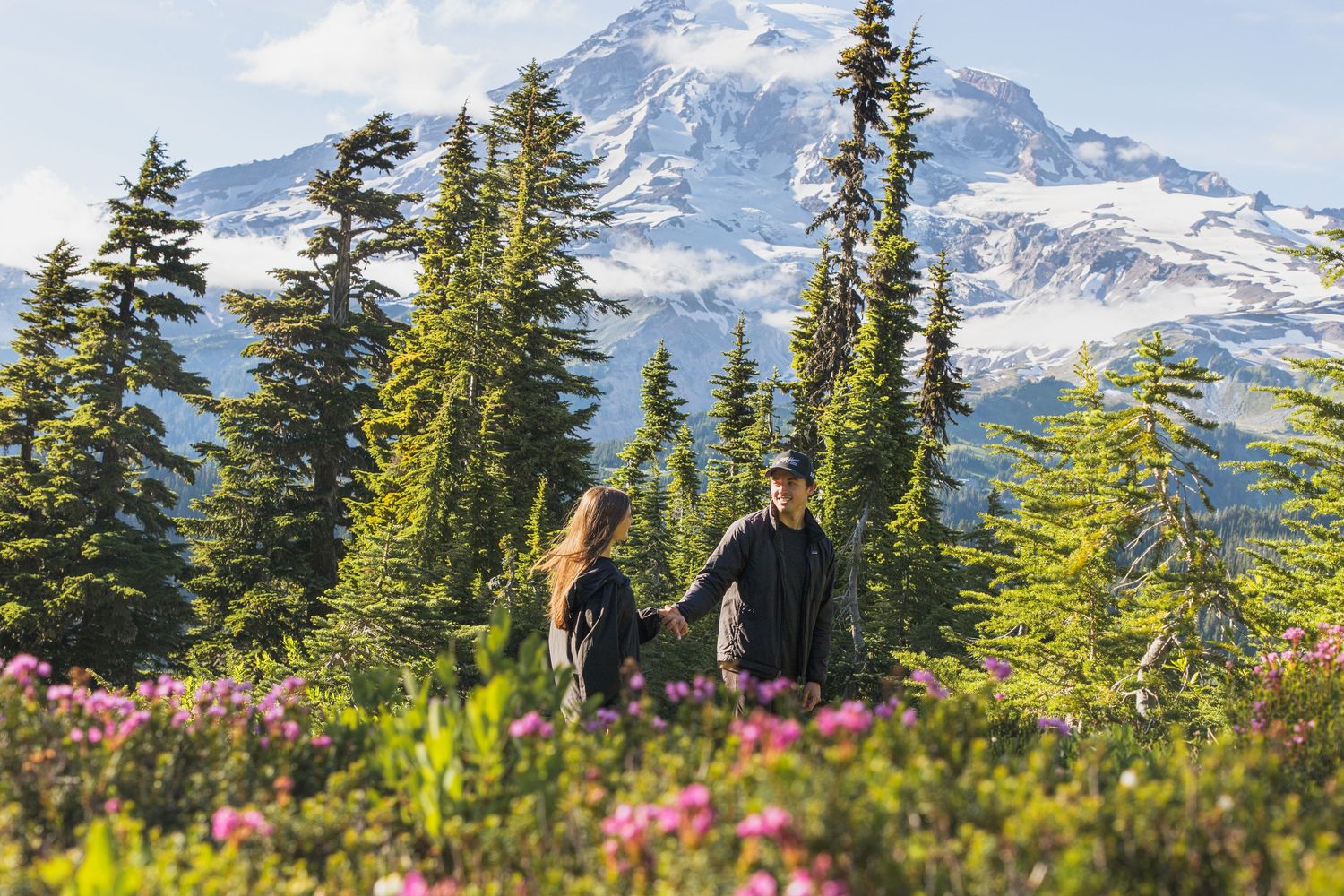 Newly engaged couple walking through wildflowers during a Mount Rainier proposal photoshoot