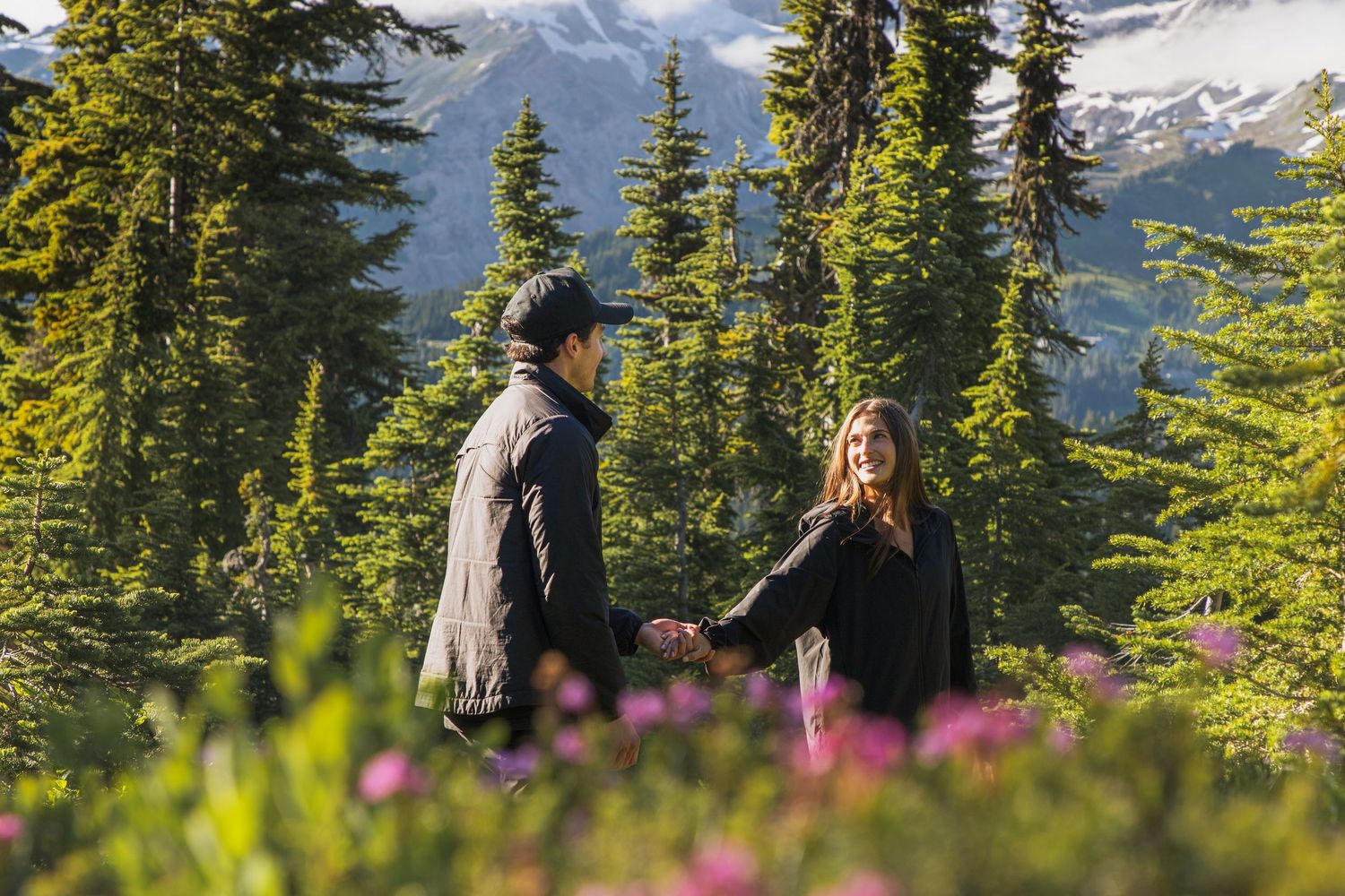 Newly engaged couple walking through wildflowers during a Mount Rainier proposal photoshoot