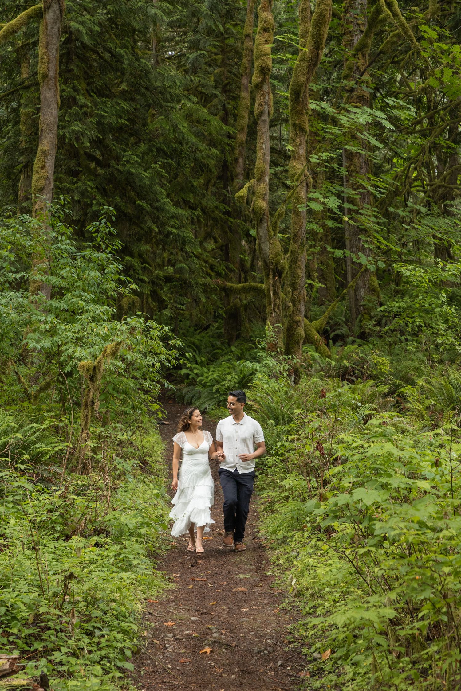 Newly engaged couple walking hand in hand through the forest near Snoqualmie Falls