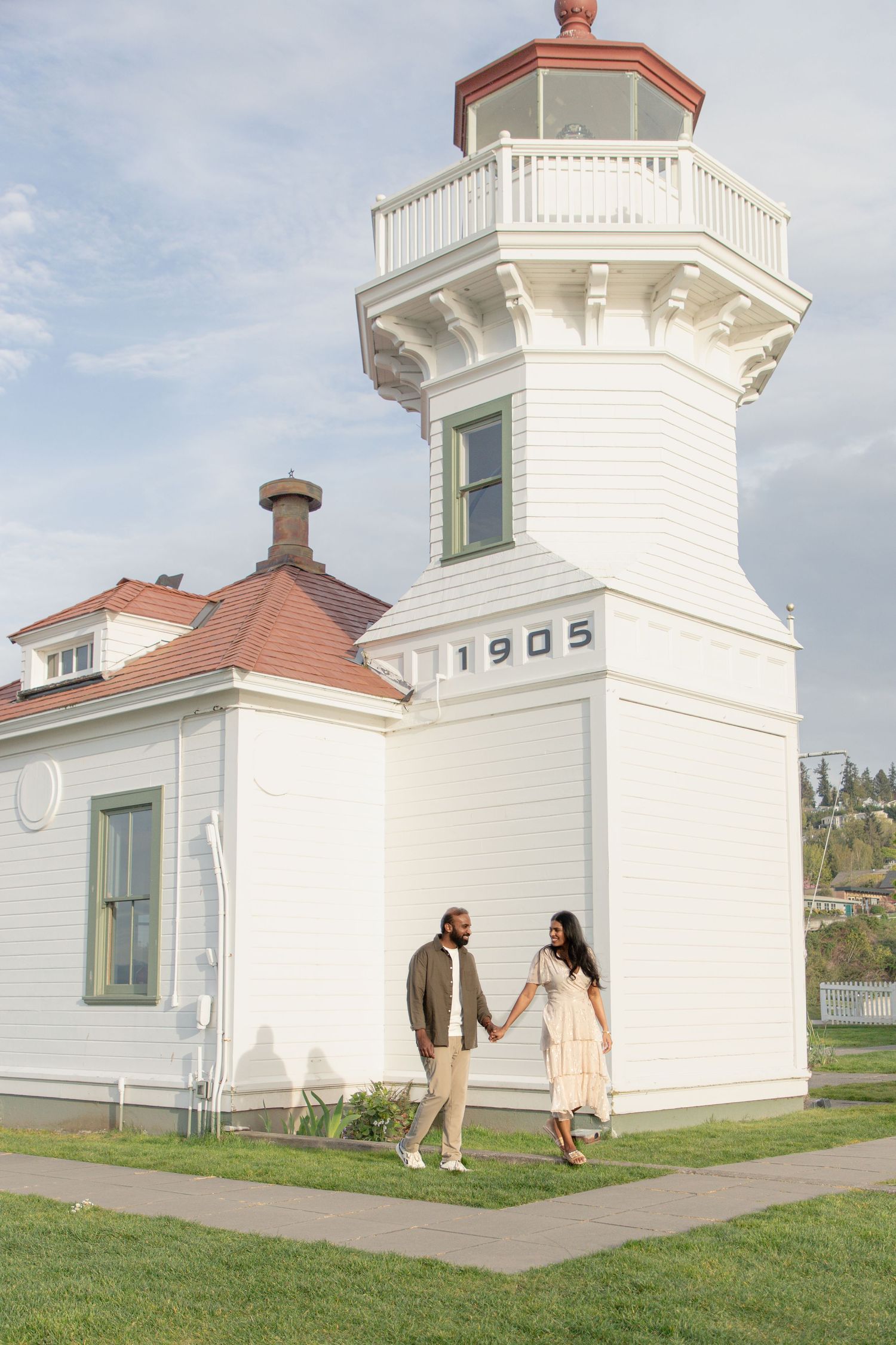 Couple walking hand in hand beside the historic Mukilteo Lighthouse after their proposal