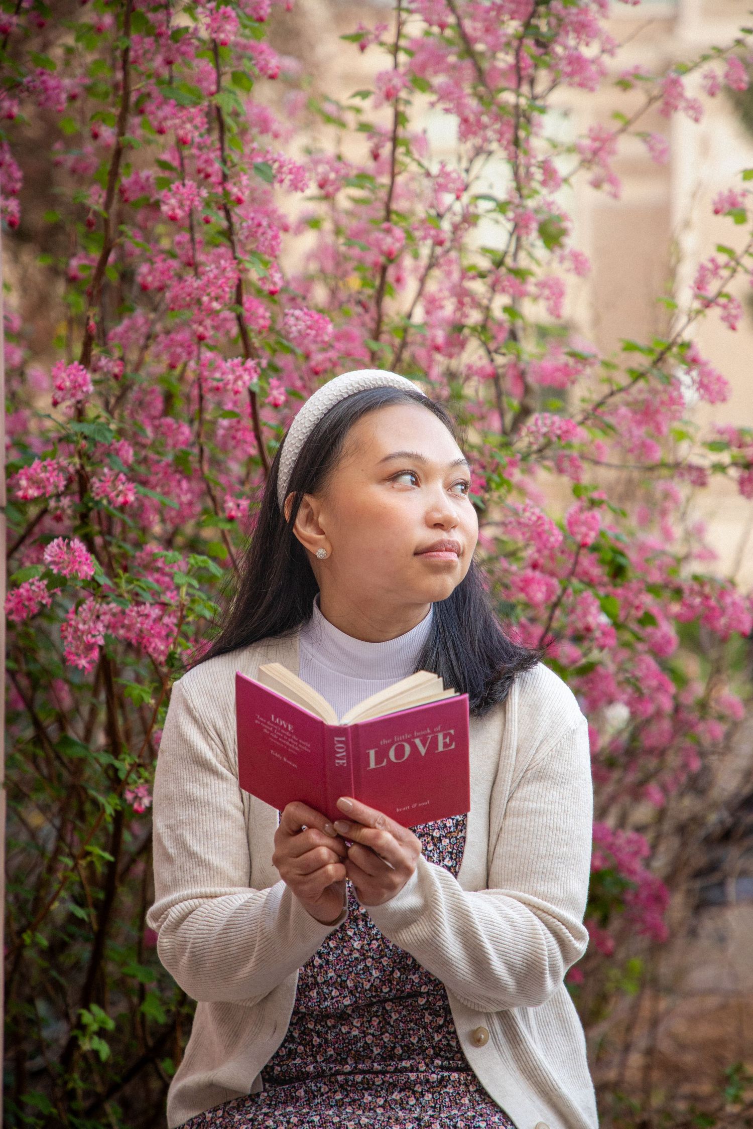 Woman reading a book surrounded by blooming pink flowers during a spring portrait session in Seattle, natural lifestyle photography
