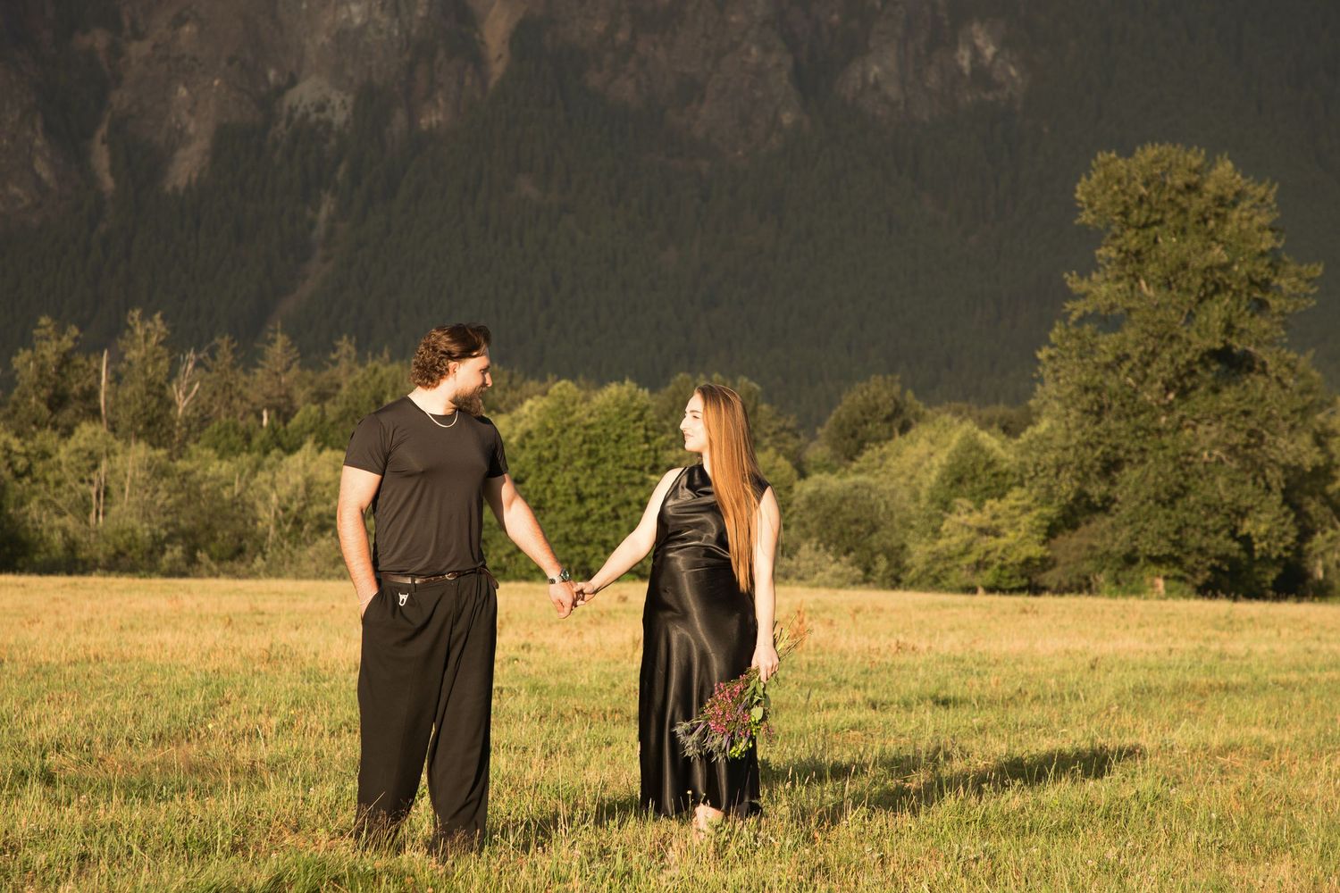 Expectant couple walking hand in hand through a meadow with elk beneath Mount Si in North Bend