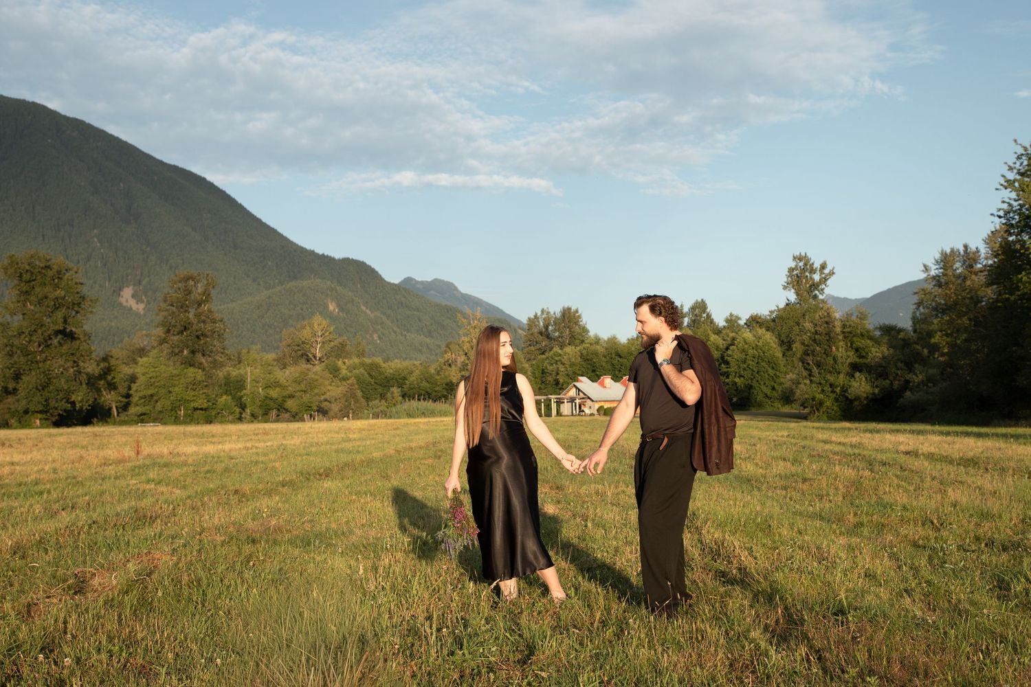 Pregnant couple holding hands and laughing in an open meadow near Mount Si in North Bend