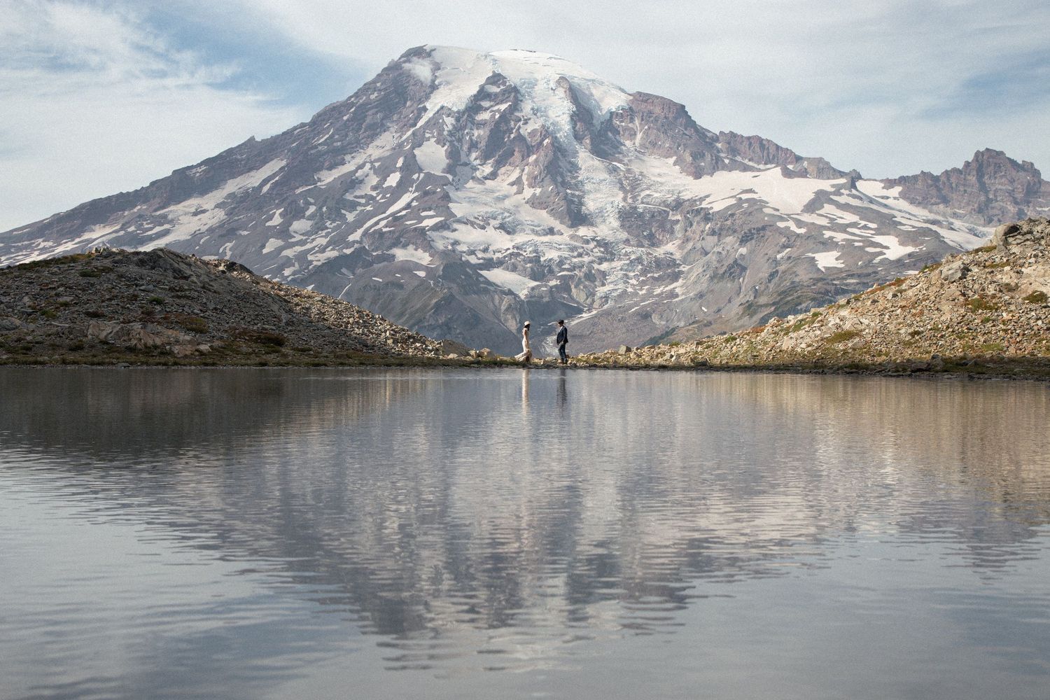 Newlyweds reflected in a calm alpine lake with Mount Rainier towering in the background