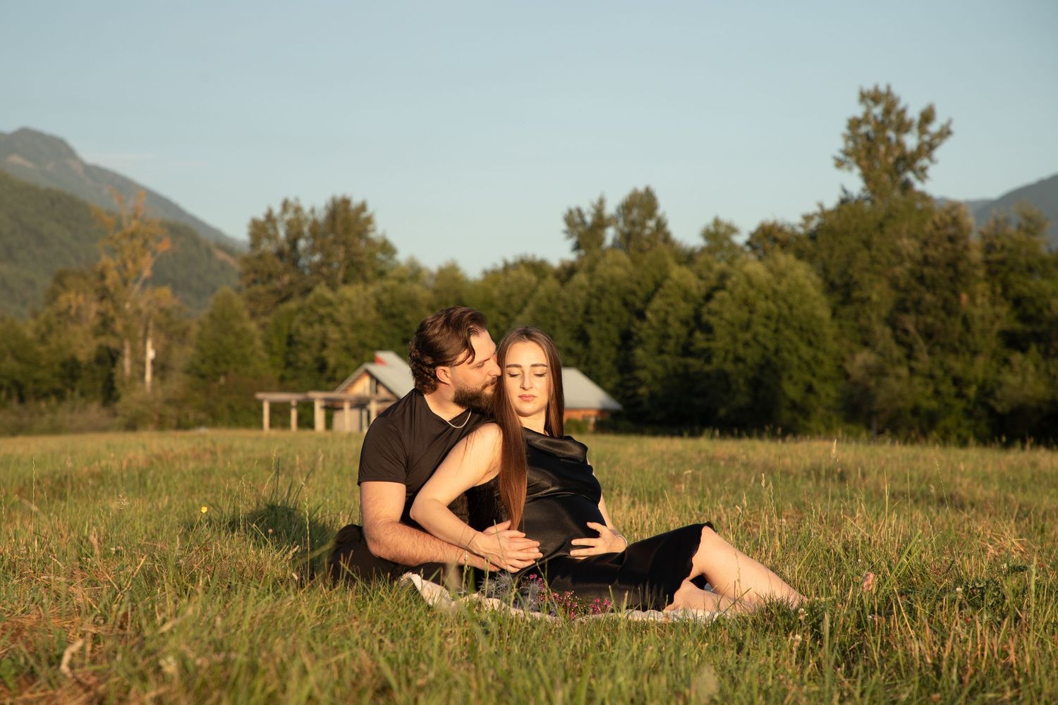 Expectant father kissing his pregnant partner as they sit together in a North Bend meadow