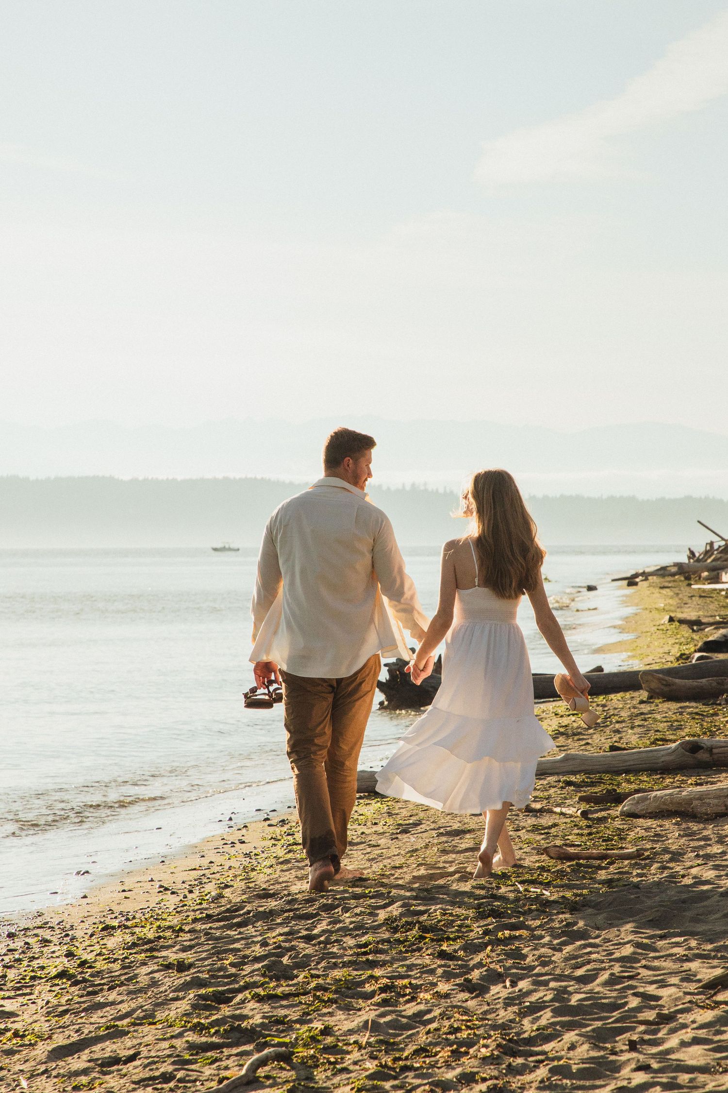 Couple photoshoot at Discovery Park during golden hour, Seattle couple walking together near the water with Puget Sound behind them