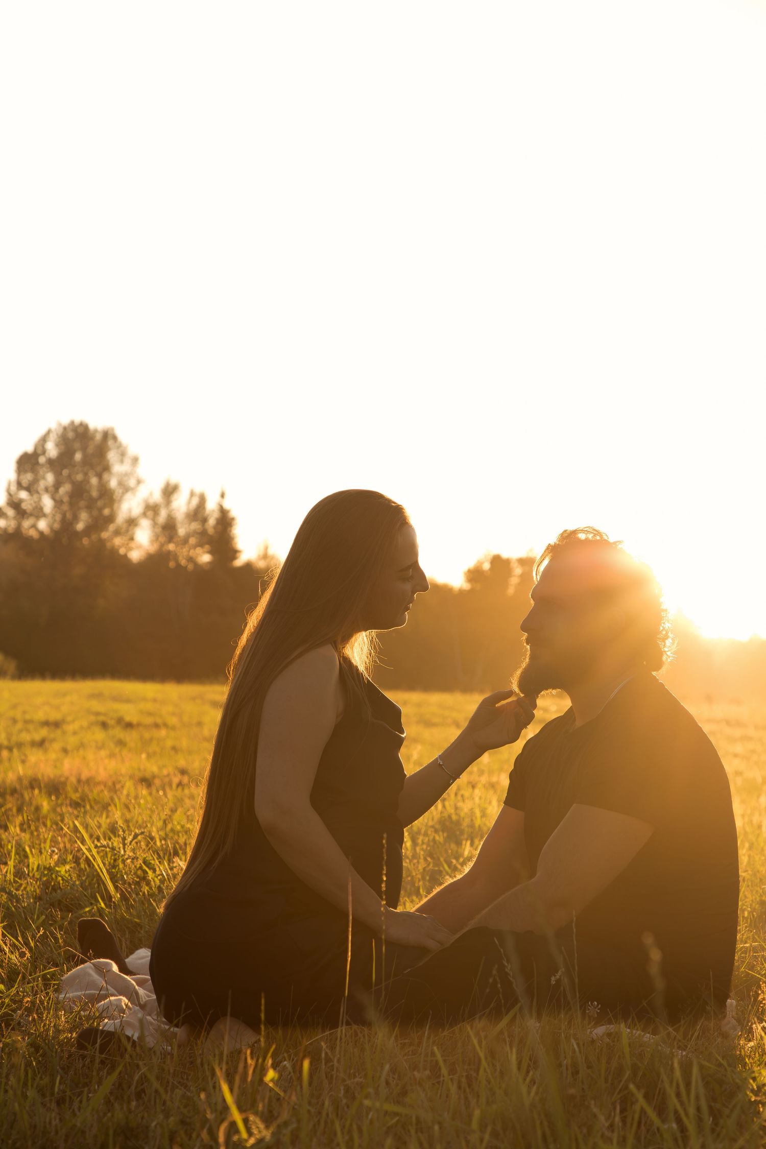 Pregnant couple sharing a tender moment in the grass at sunset during their North Bend maternity session