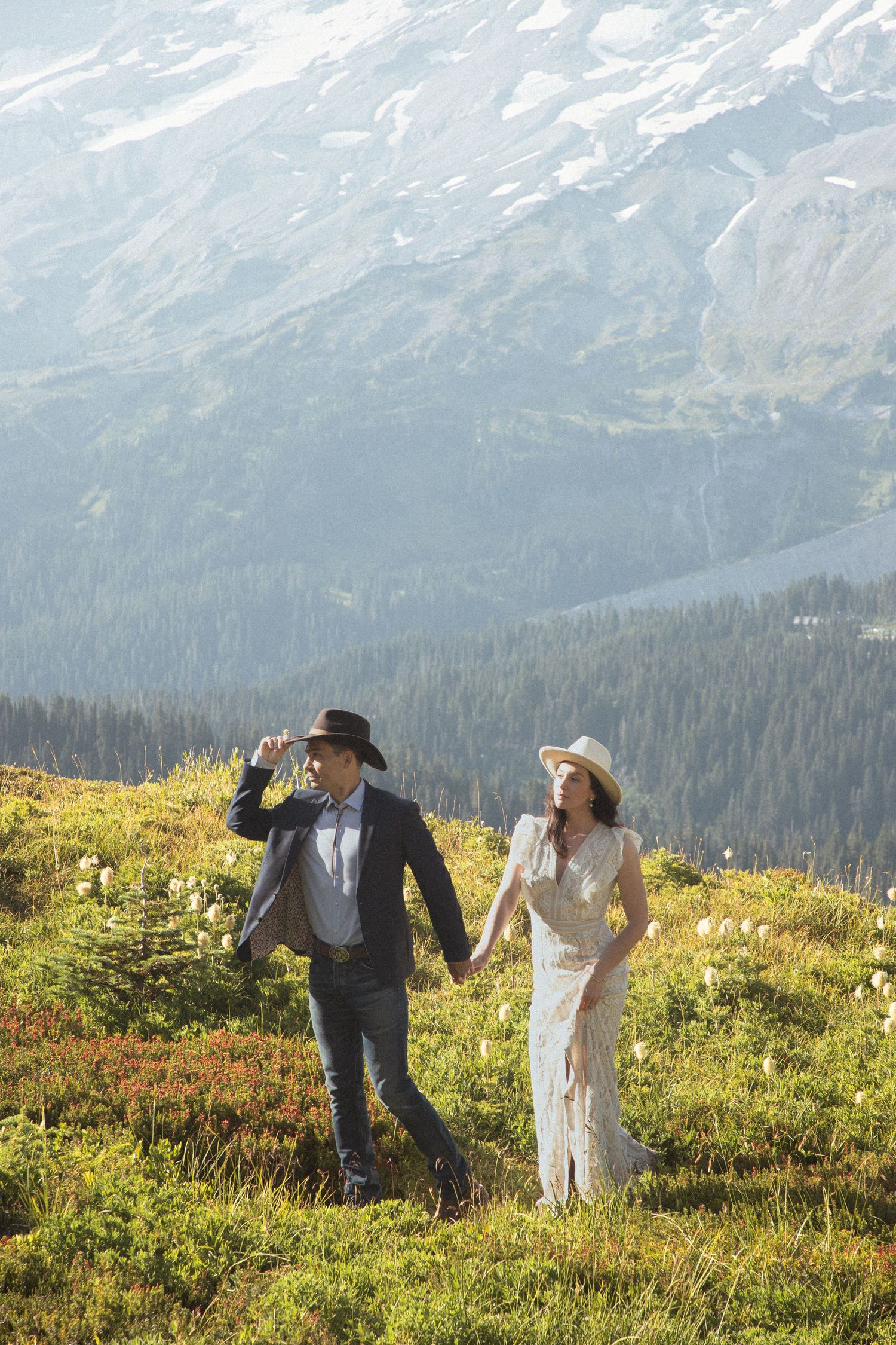 Newlyweds walking hand in hand through an alpine meadow with Mount Rainier in the background