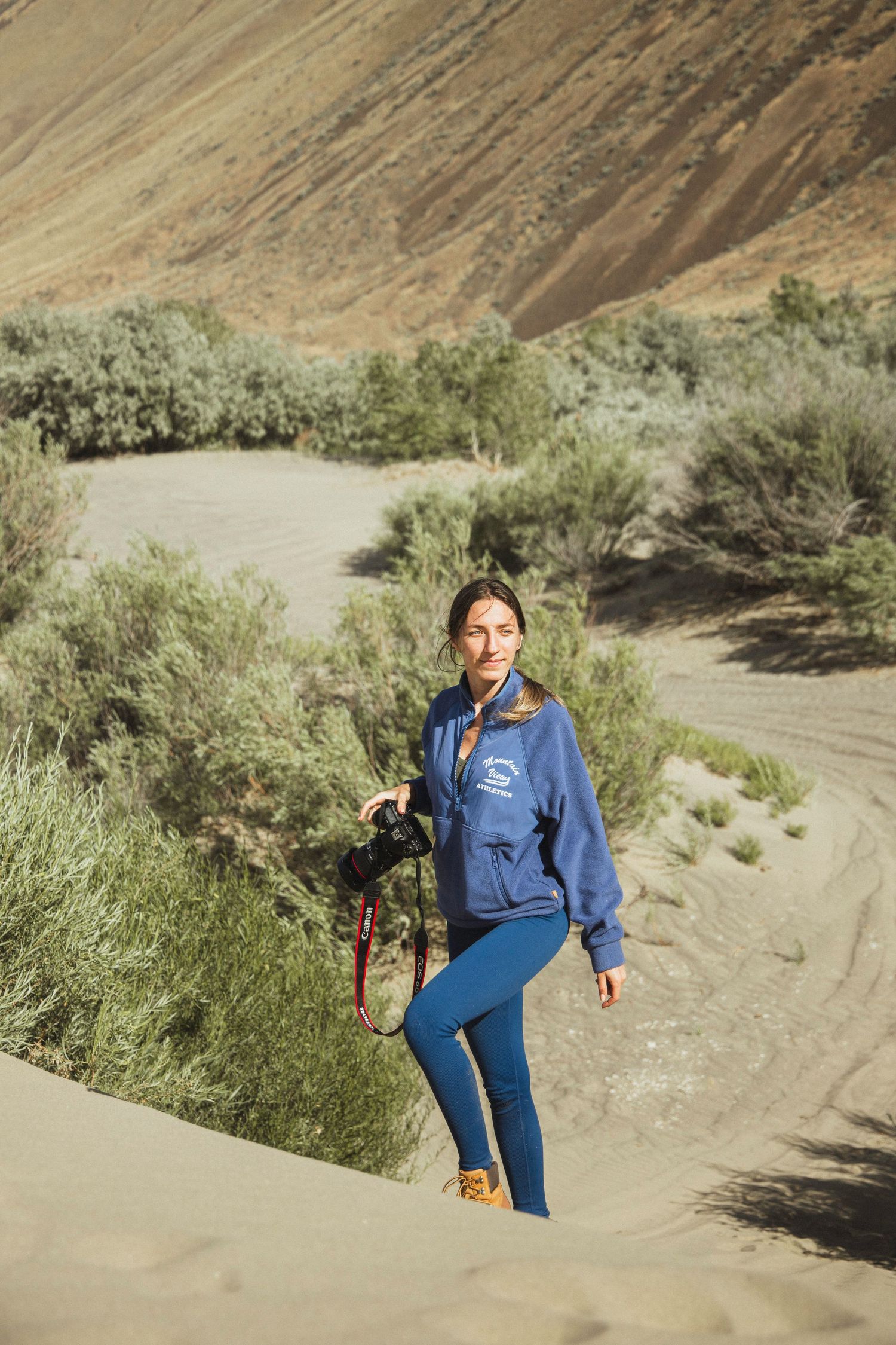 Seattle photographer walking with a camera in a desert‑style landscape during a creative portrait session