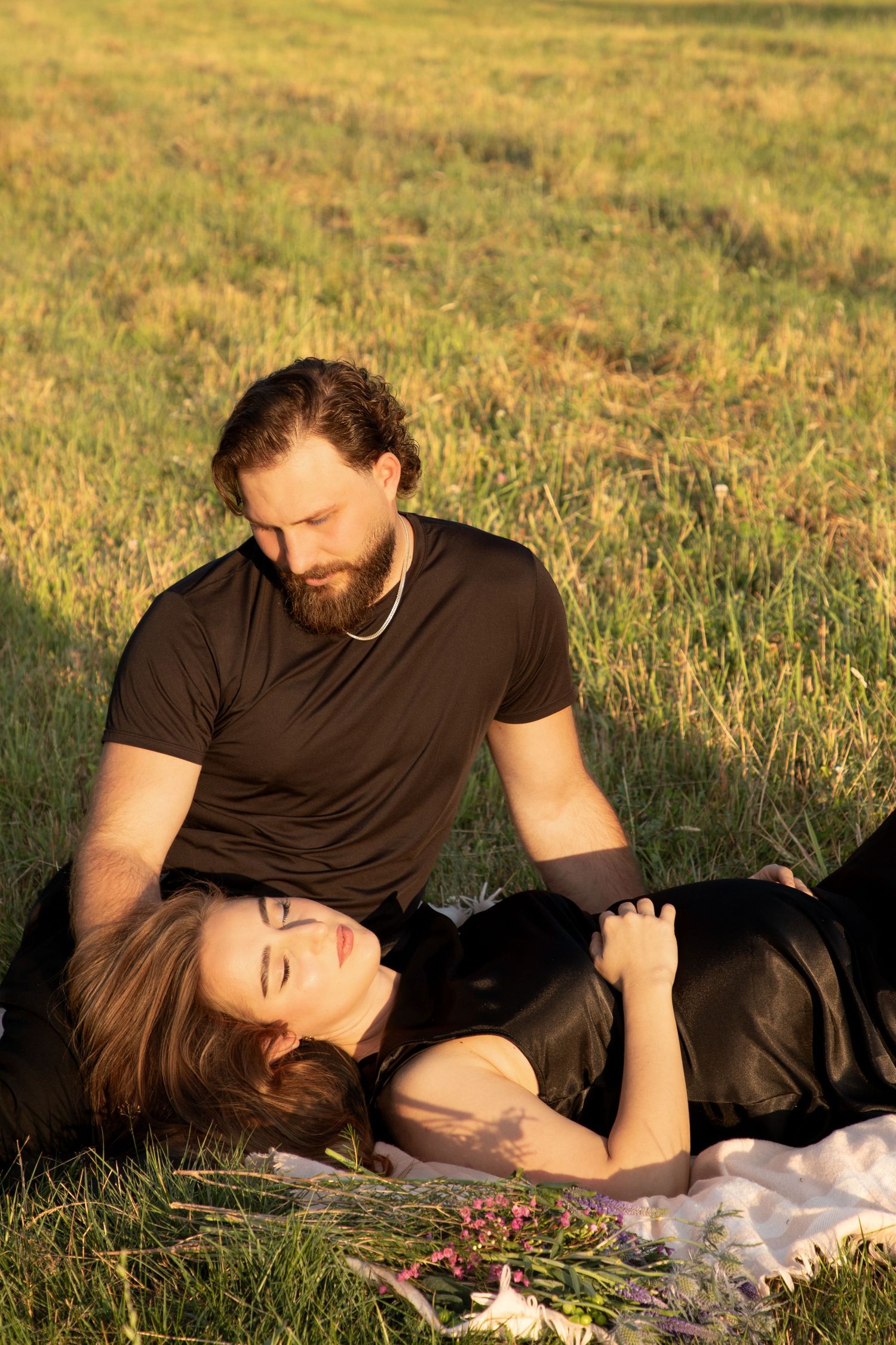 Partner resting beside the pregnant mother in the grass during an intimate outdoor maternity session