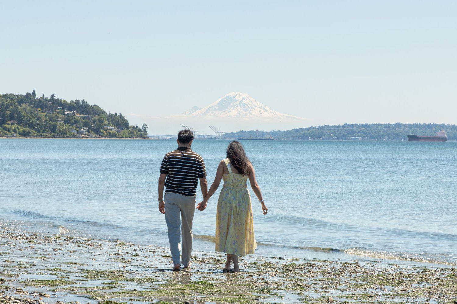 Couple walking hand in hand along the beach with Mount Rainier during a Discovery Park proposal photoshoot