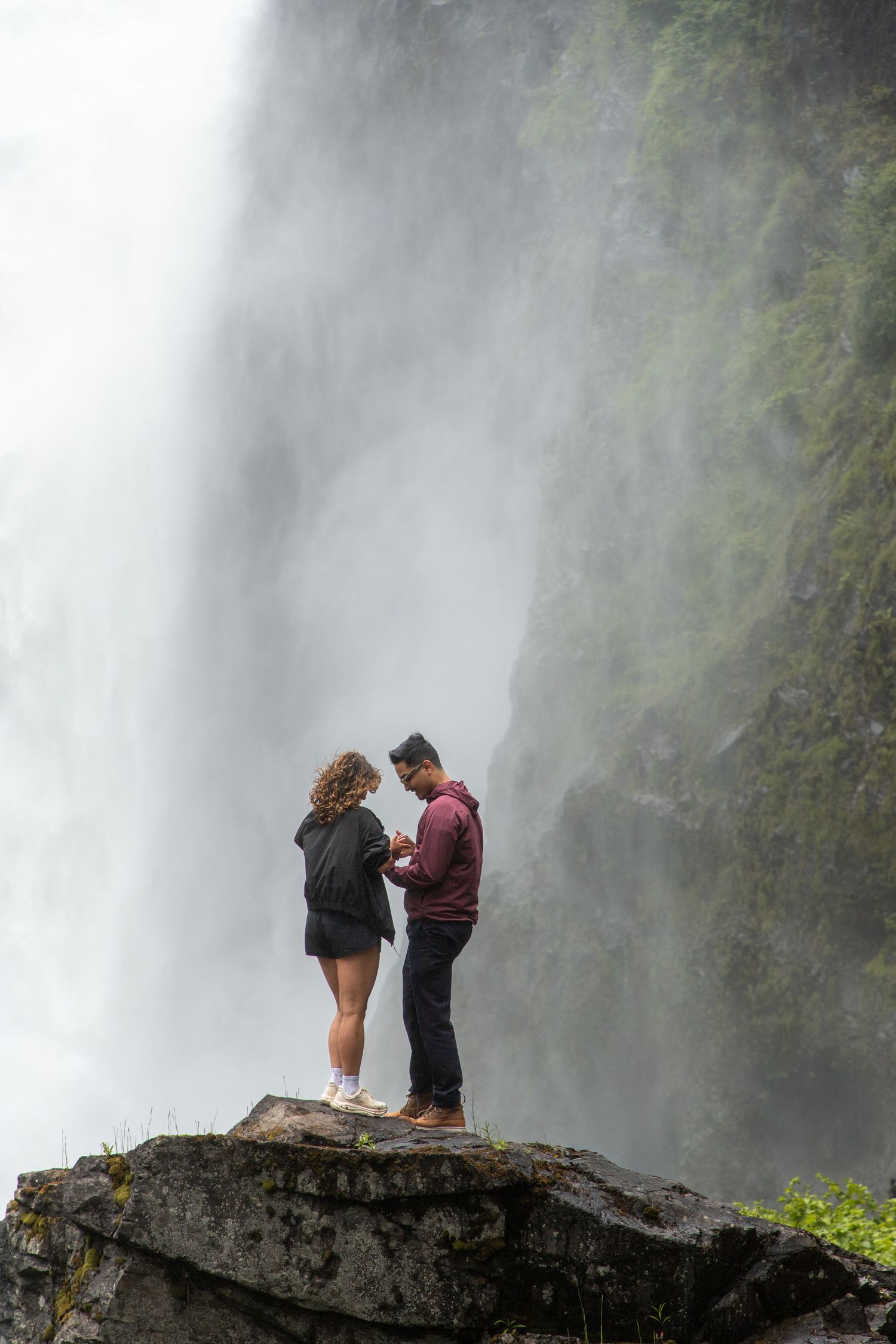 Couple sharing an emotional moment on a rock during a surprise proposal at Snoqualmie Falls