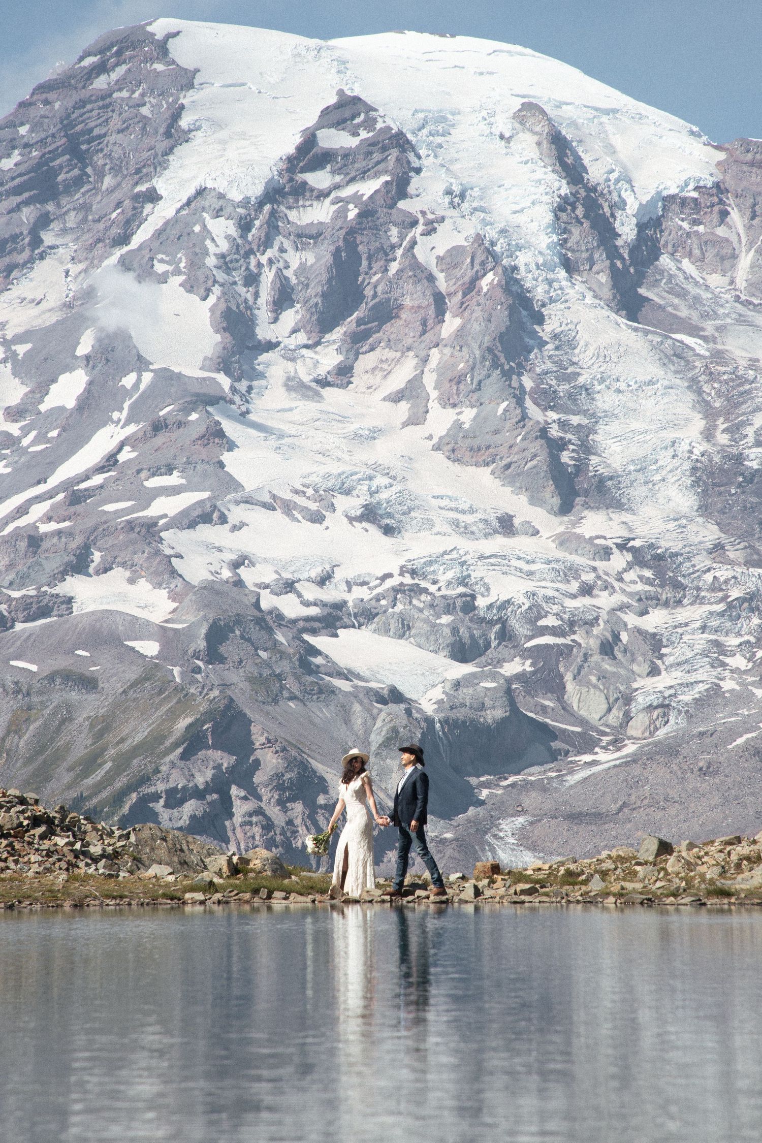 Newlyweds standing at the edge of a reflective alpine lake beneath Mount Rainier