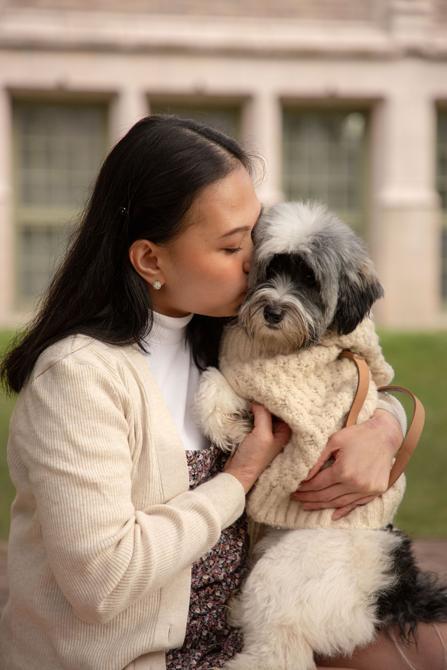 Woman holding and kissing her dog during a spring portrait session at the University of Washington cherry blossoms in Seattle