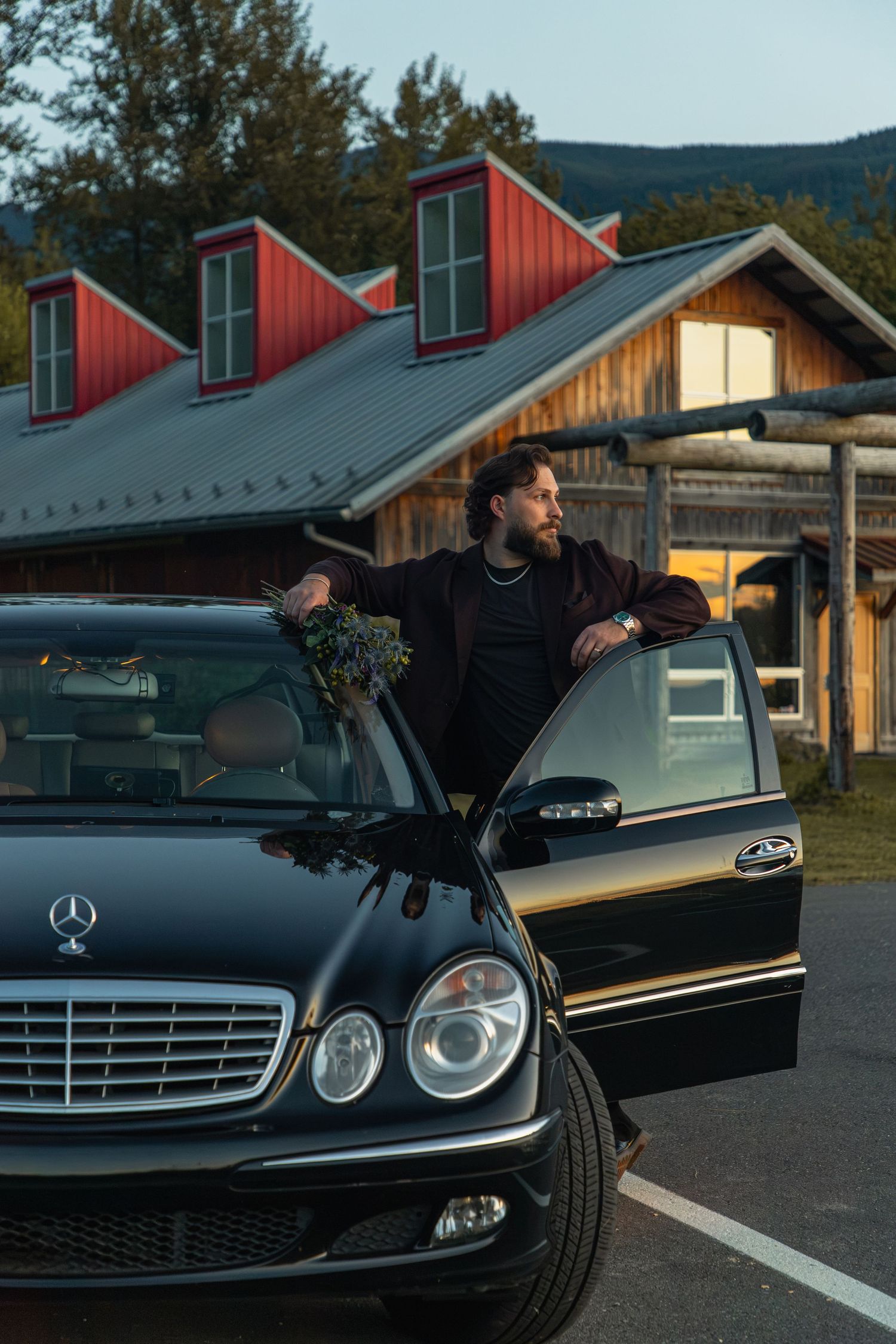 Expectant parents embracing behind a classic Mercedes outside a rustic North Bend lodge