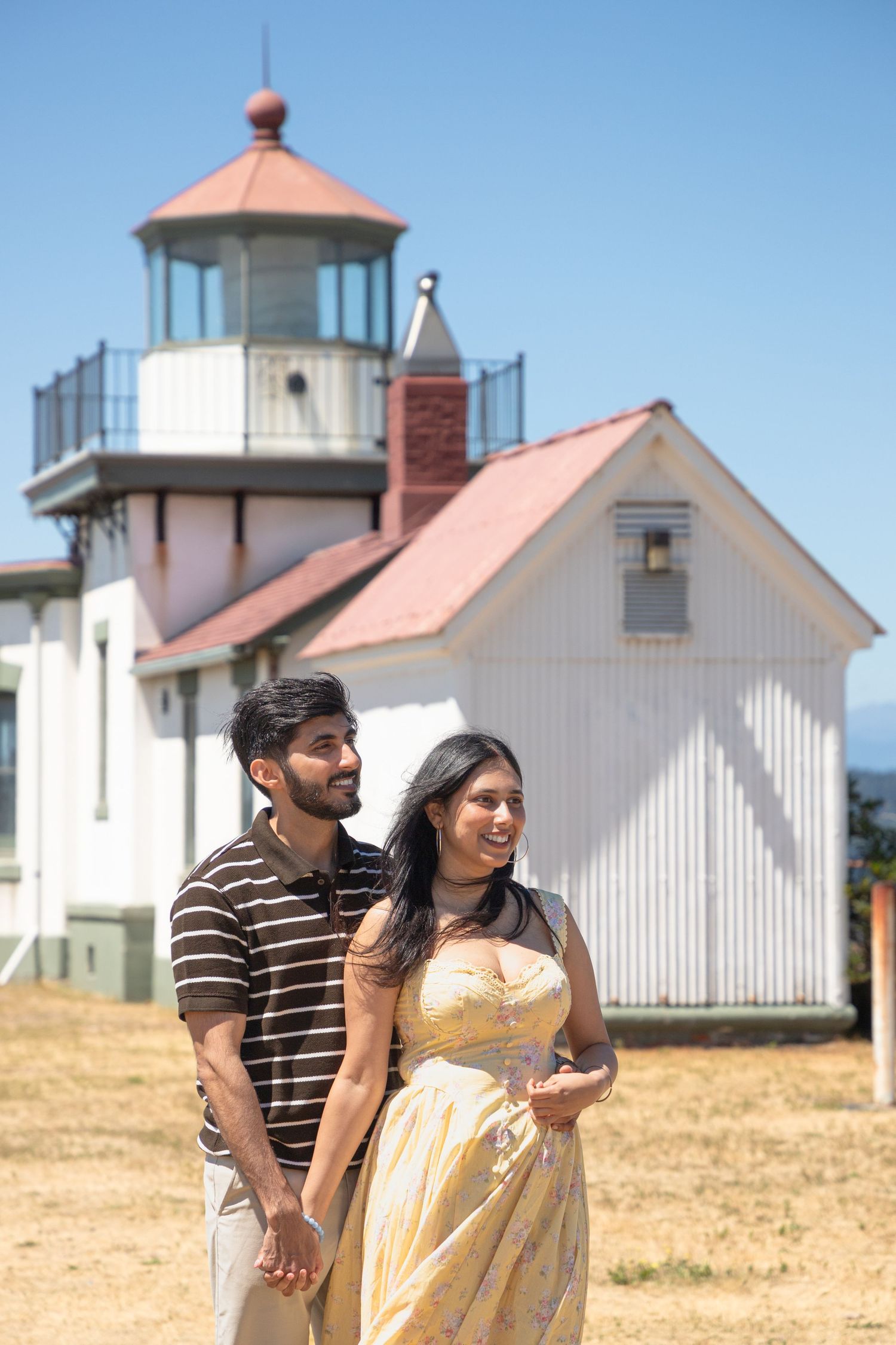 Newly engaged couple walking hand in hand near West Point Lighthouse at Discovery Park