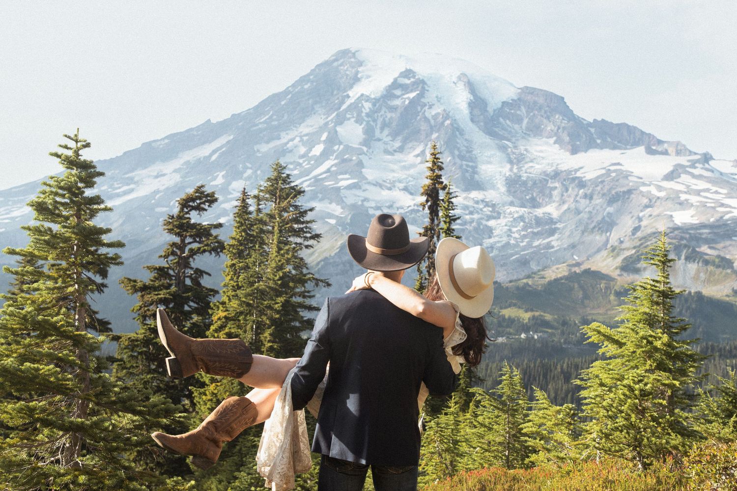 Groom carrying the bride among evergreens with snow-covered Mount Rainier rising behind them