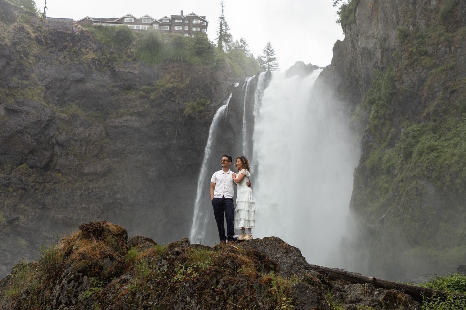 Engaged couple posing on a rocky overlook during their Snoqualmie Falls proposal session