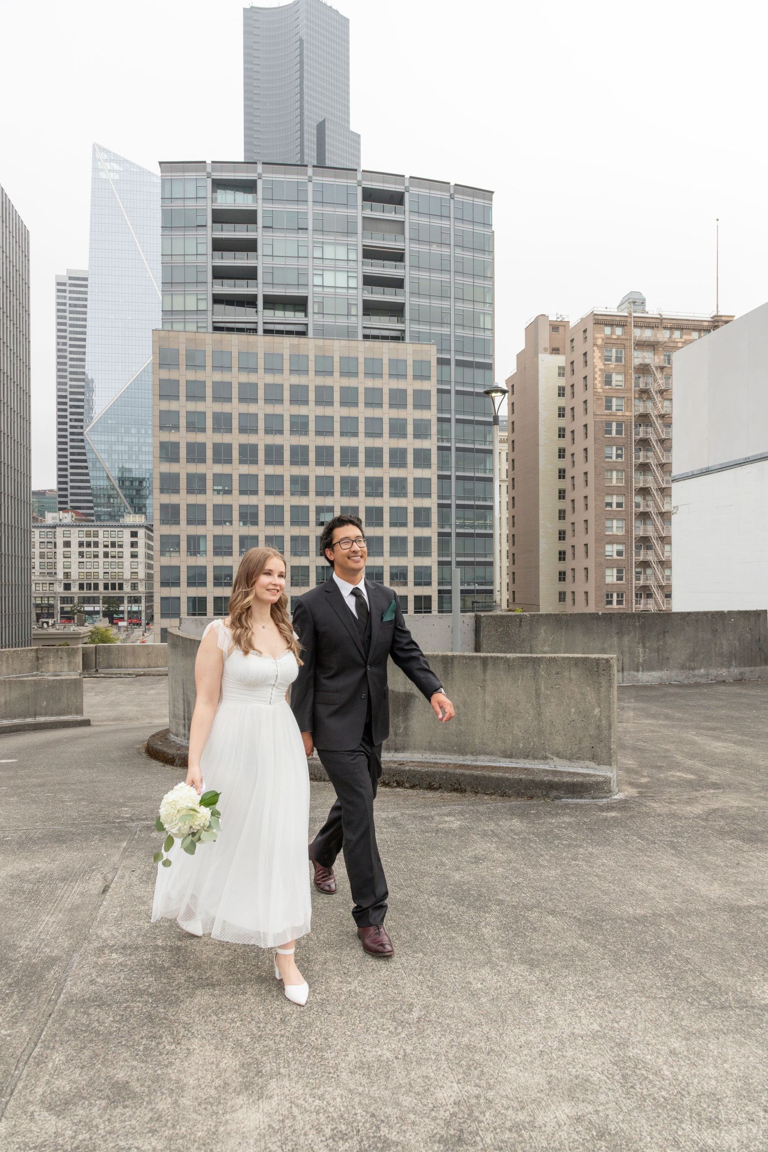 Bride and groom walking across a downtown Seattle rooftop after their intimate courthouse wedding ceremony