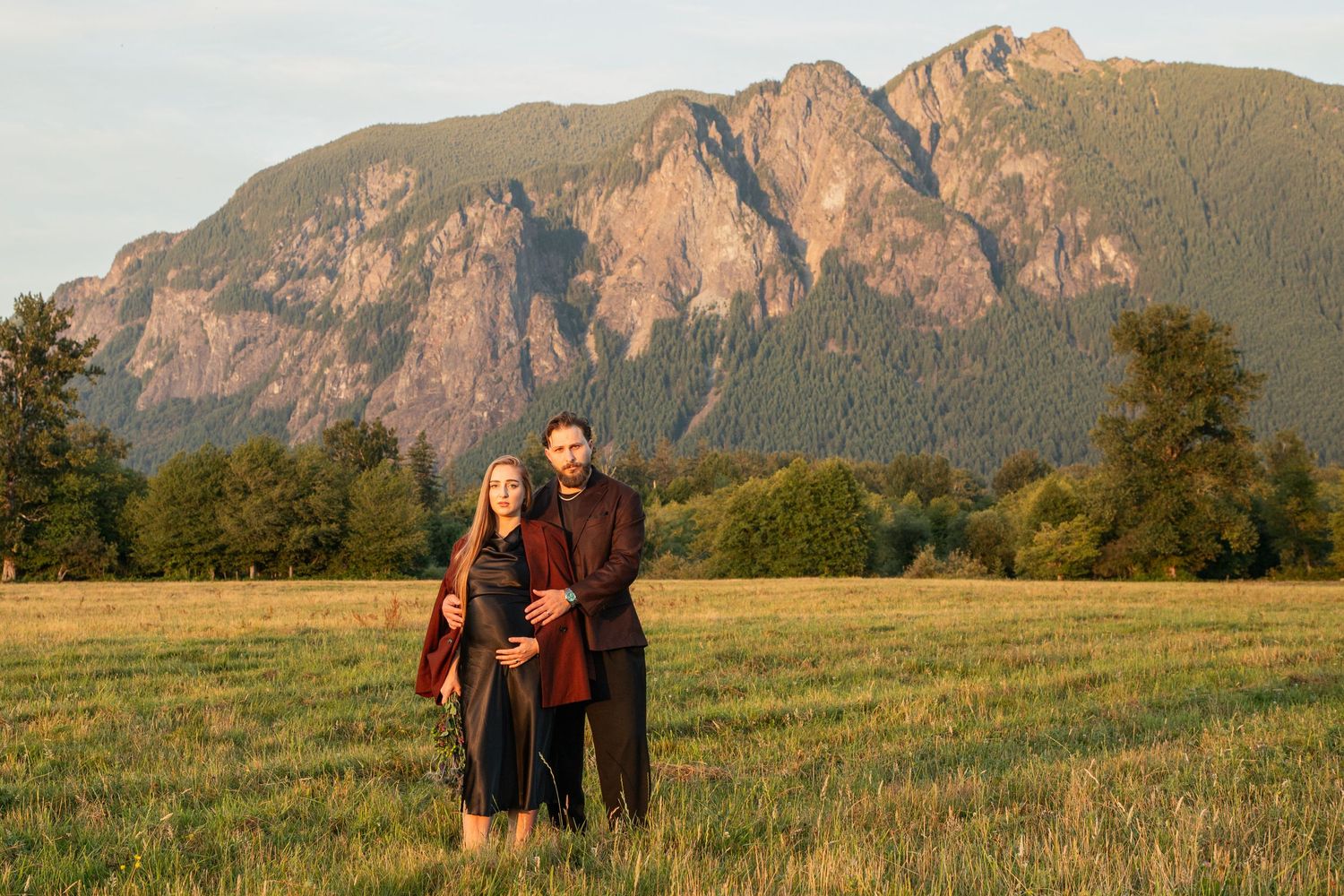 Expectant parents standing together in a wide meadow beneath Mount Si in North Bend