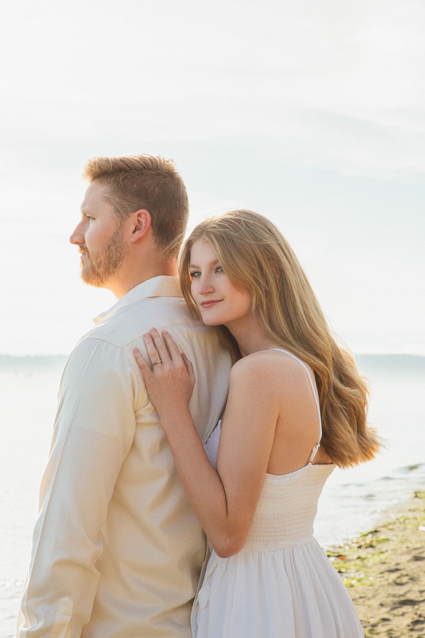Romantic golden hour couple portraits at Discovery Park, Seattle couple embracing with soft light and Puget Sound in the distance