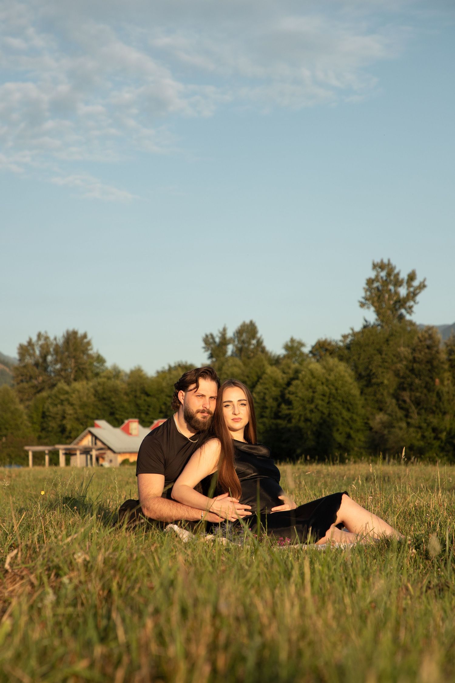 Expectant couple cuddling in tall grass during a relaxed North Bend maternity photoshoot