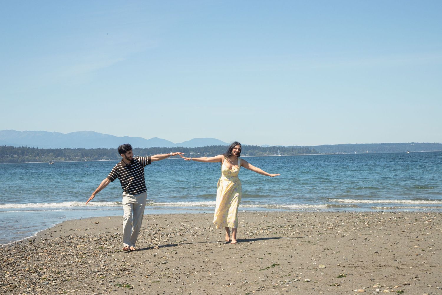 Newly engaged couple running along the beach during a proposal session at Discovery Park in Seattle