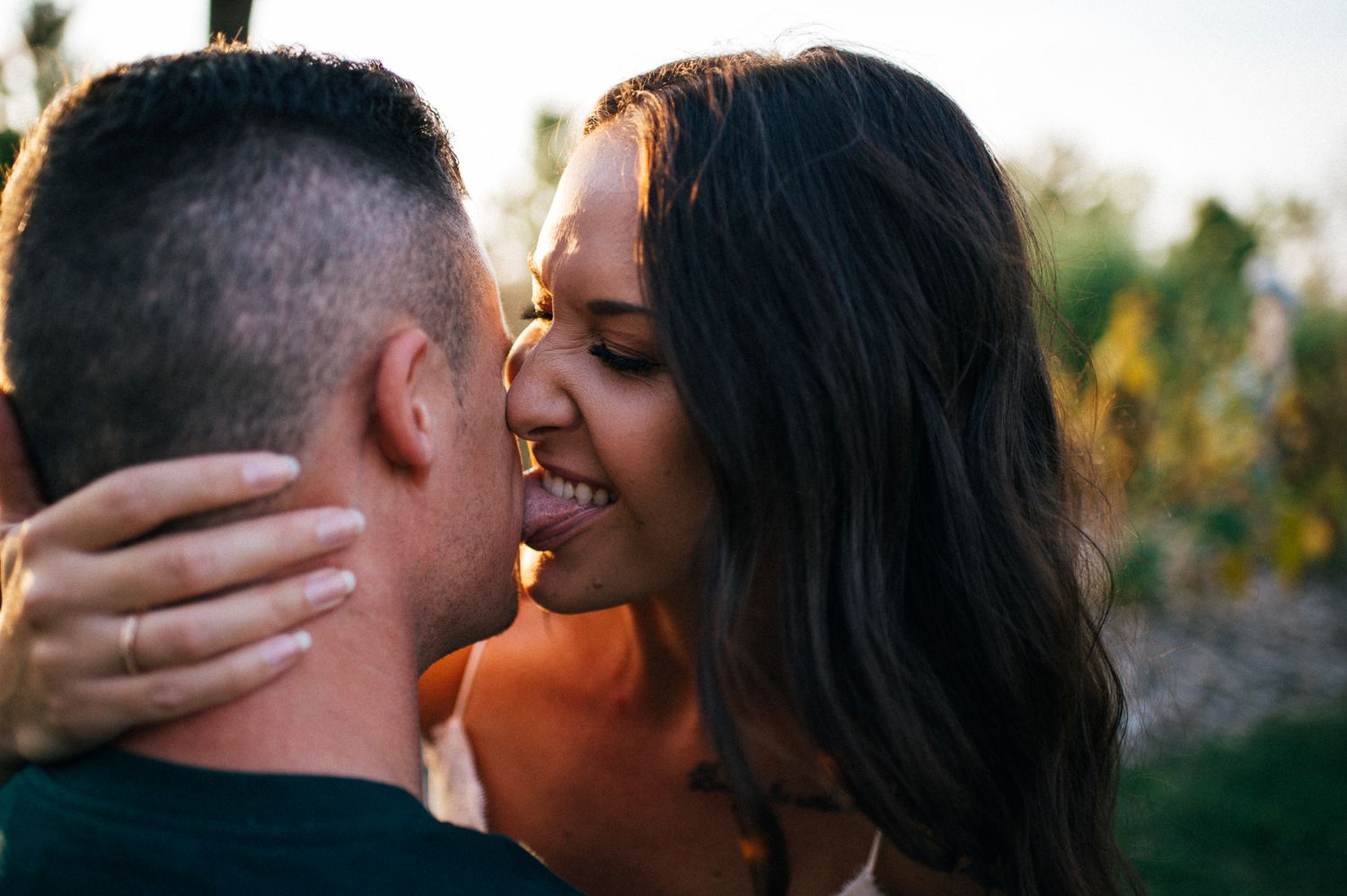 Intimate couple sharing a tender kiss outdoors during golden hour.