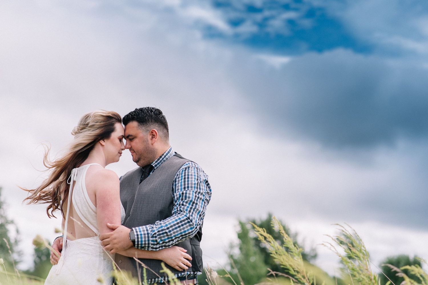 Romantic couple's photo session against dramatic cloudy sky in an open field.