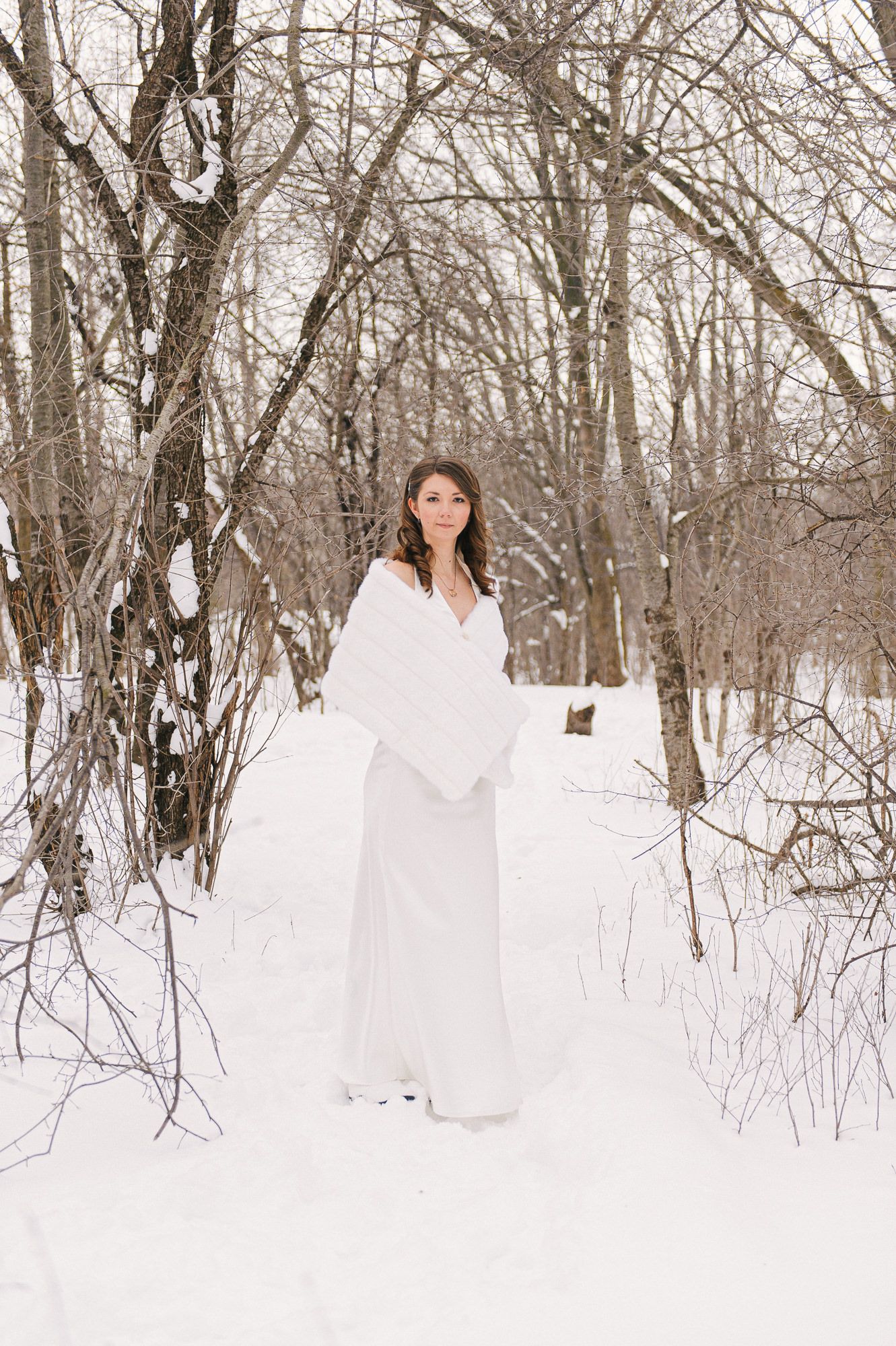 Woman in white dress walking through snowy winter forest landscape.