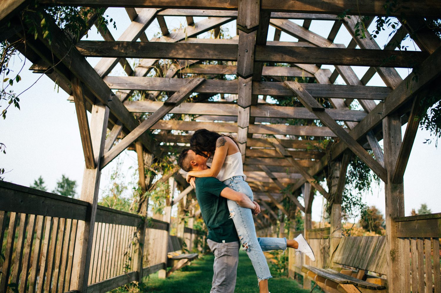 A romantic couple embraces under a rustic wooden pergola during a sunset photoshoot.