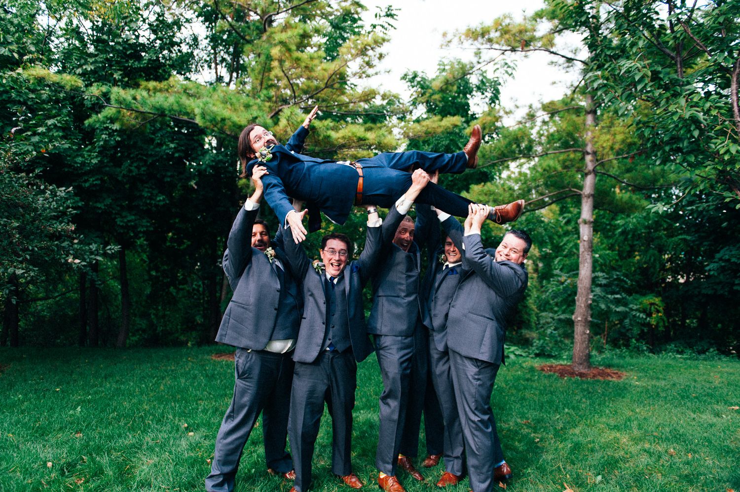 Groomsmen in gray suits celebrating outdoors on a sunny day.