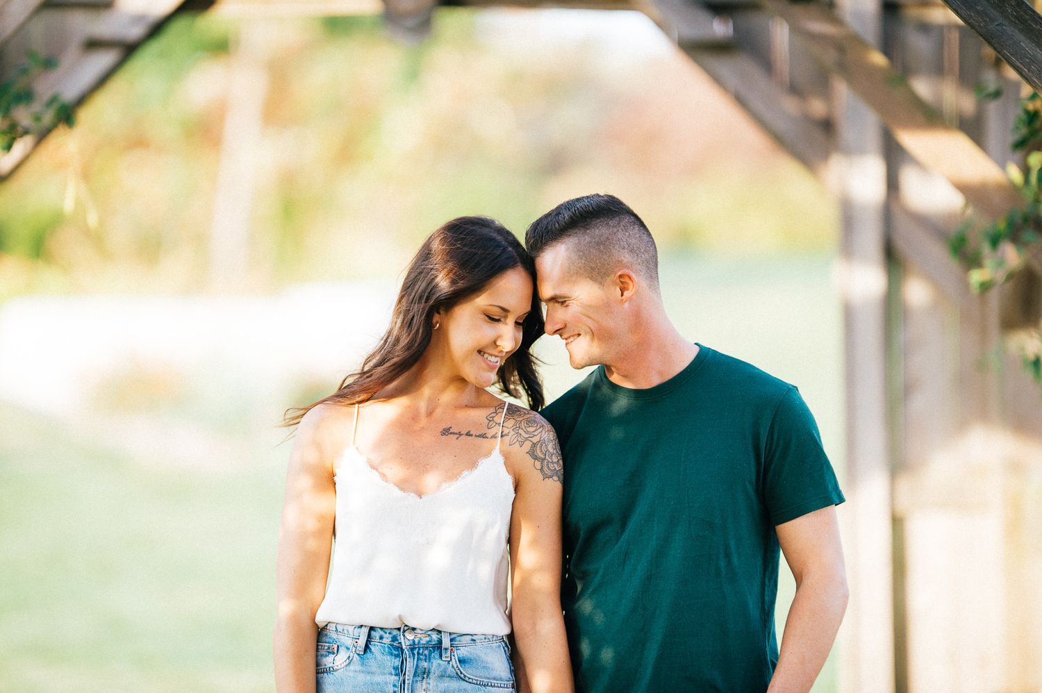 A couple shares a tender moment under a wooden pergola in soft natural light.
