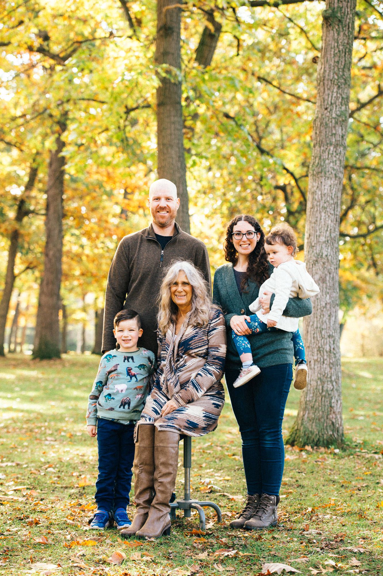 Family group sitting together on fallen leaves during autumn photo session.
