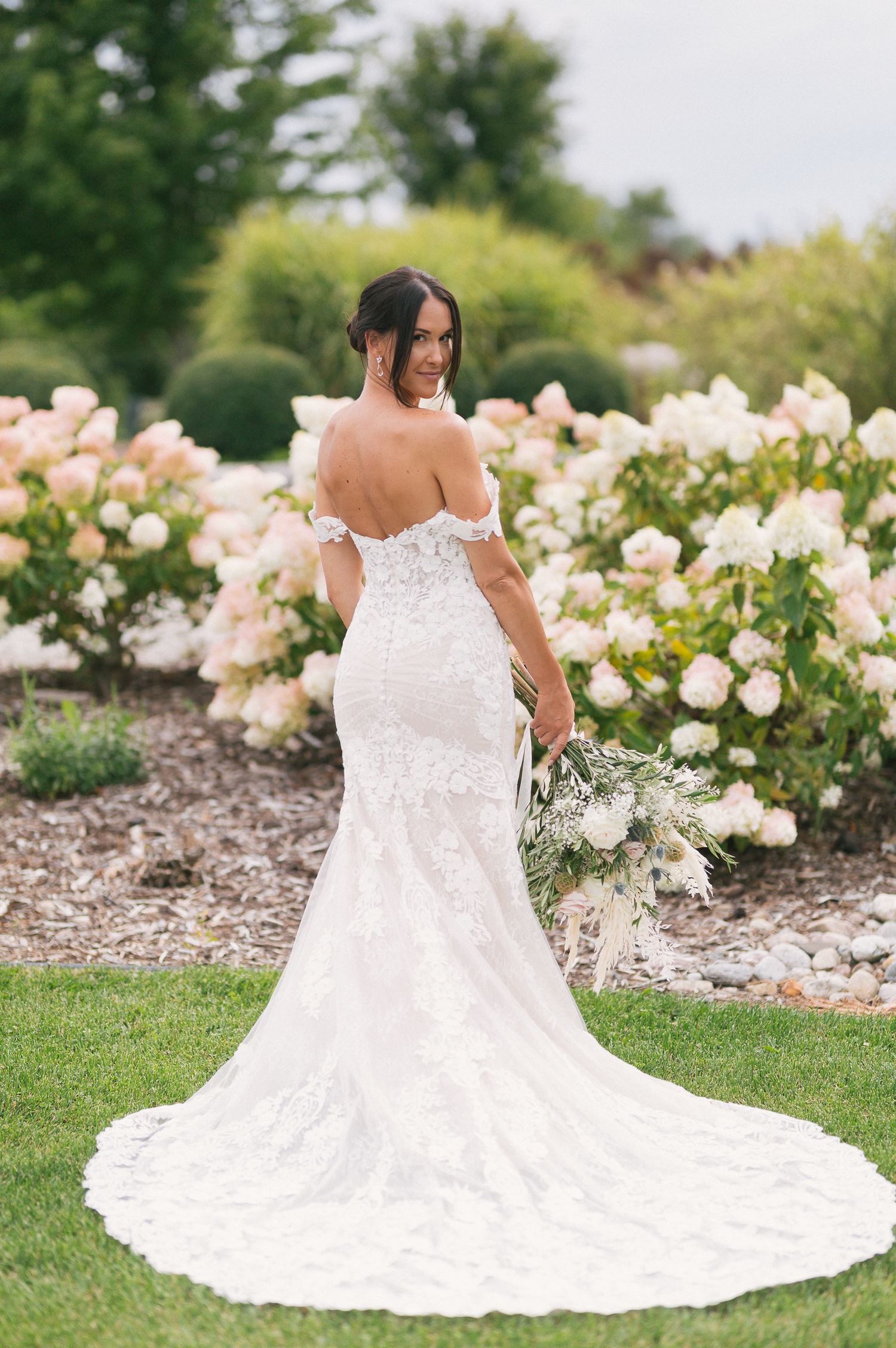 Elegant lace wedding dress with long train photographed in a rose garden.