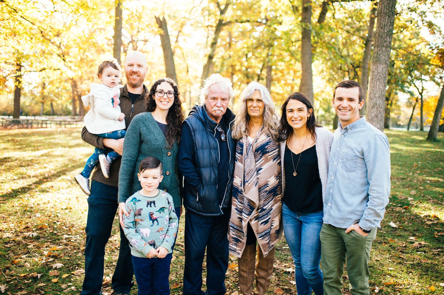Large family gathering in a sunny autumn park with golden sunlight filtering through trees.